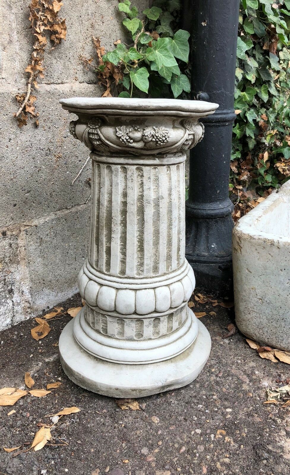 Decorative stone pedestal with carved floral accents and fluted column, designed to support garden statues or outdoor planters.