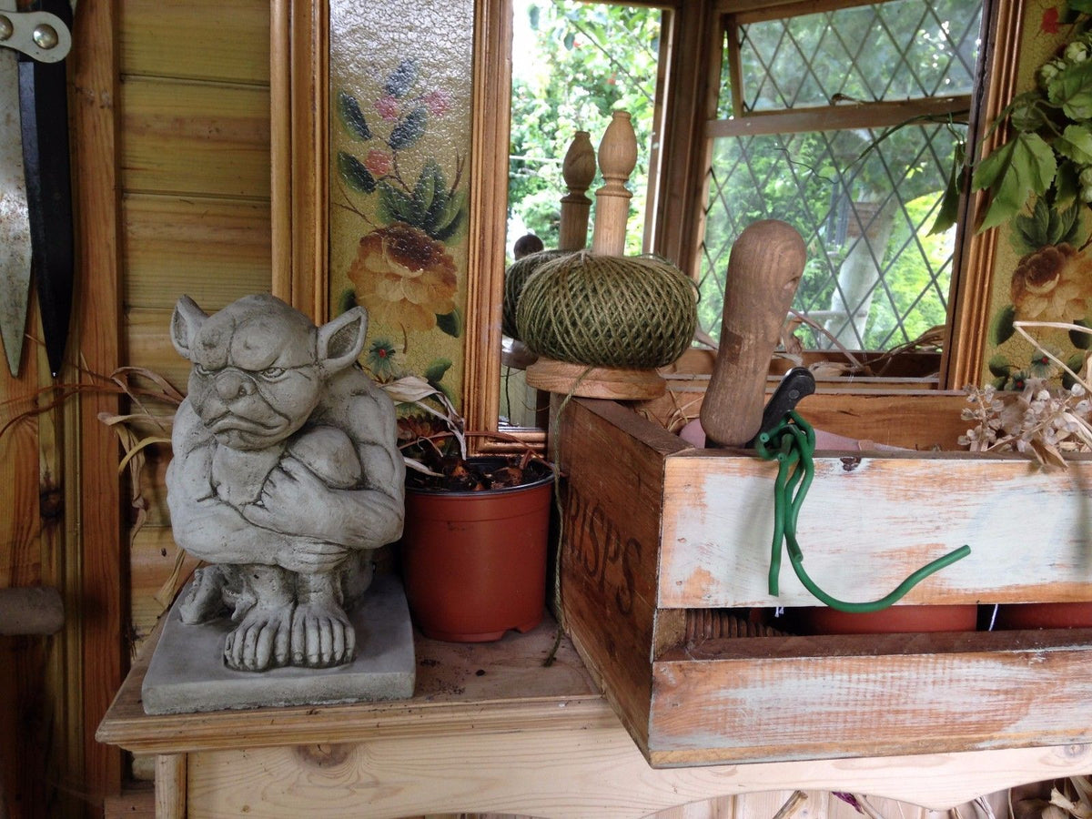 Grumpy Gargoyle Statue displayed indoors on rustic shelf with garden tools. Versatile gothic decor for home or garden.