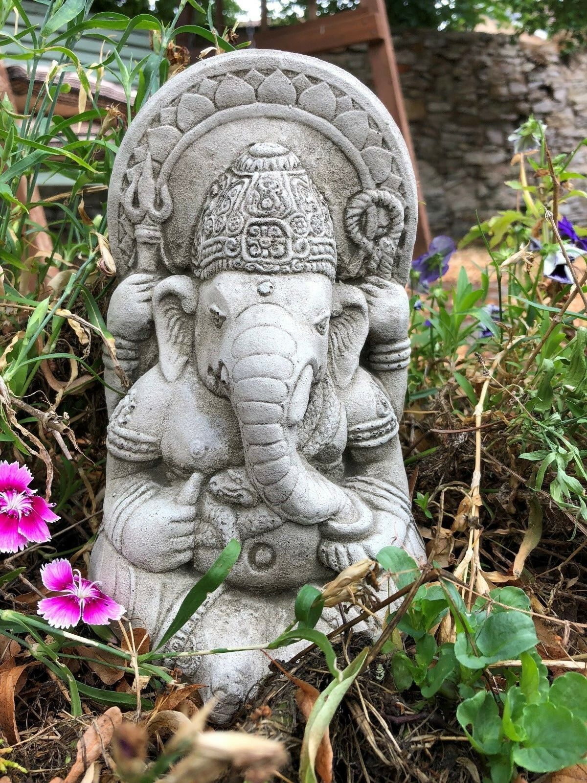 Detailed front view of Ganesh Garden Ornament - Small Stone among garden flowers. Durable and weatherproof limestone statue.