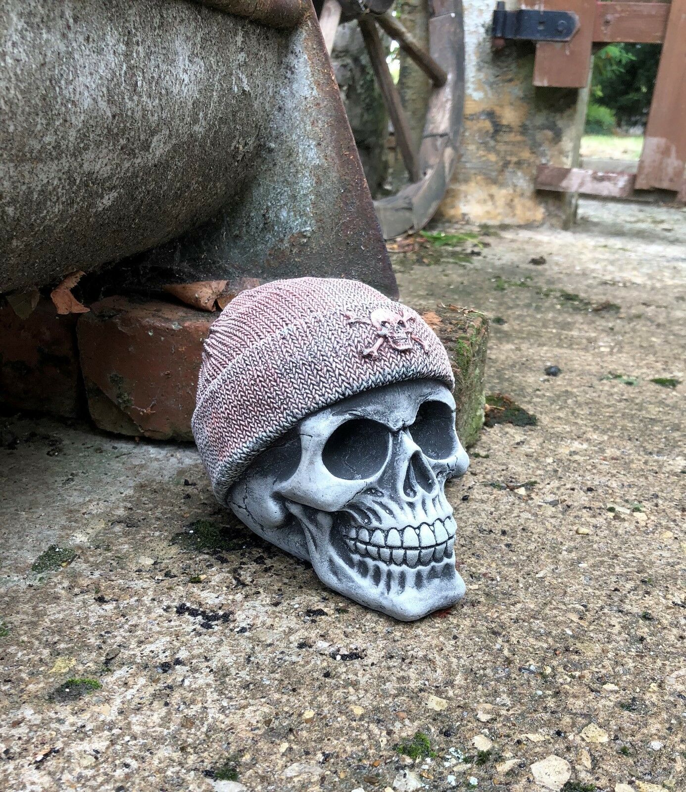 Side view of Stone Skull Beanie Ornament placed on patio, showcasing realistic limestone texture and antique finish for outdoor garden decoration.