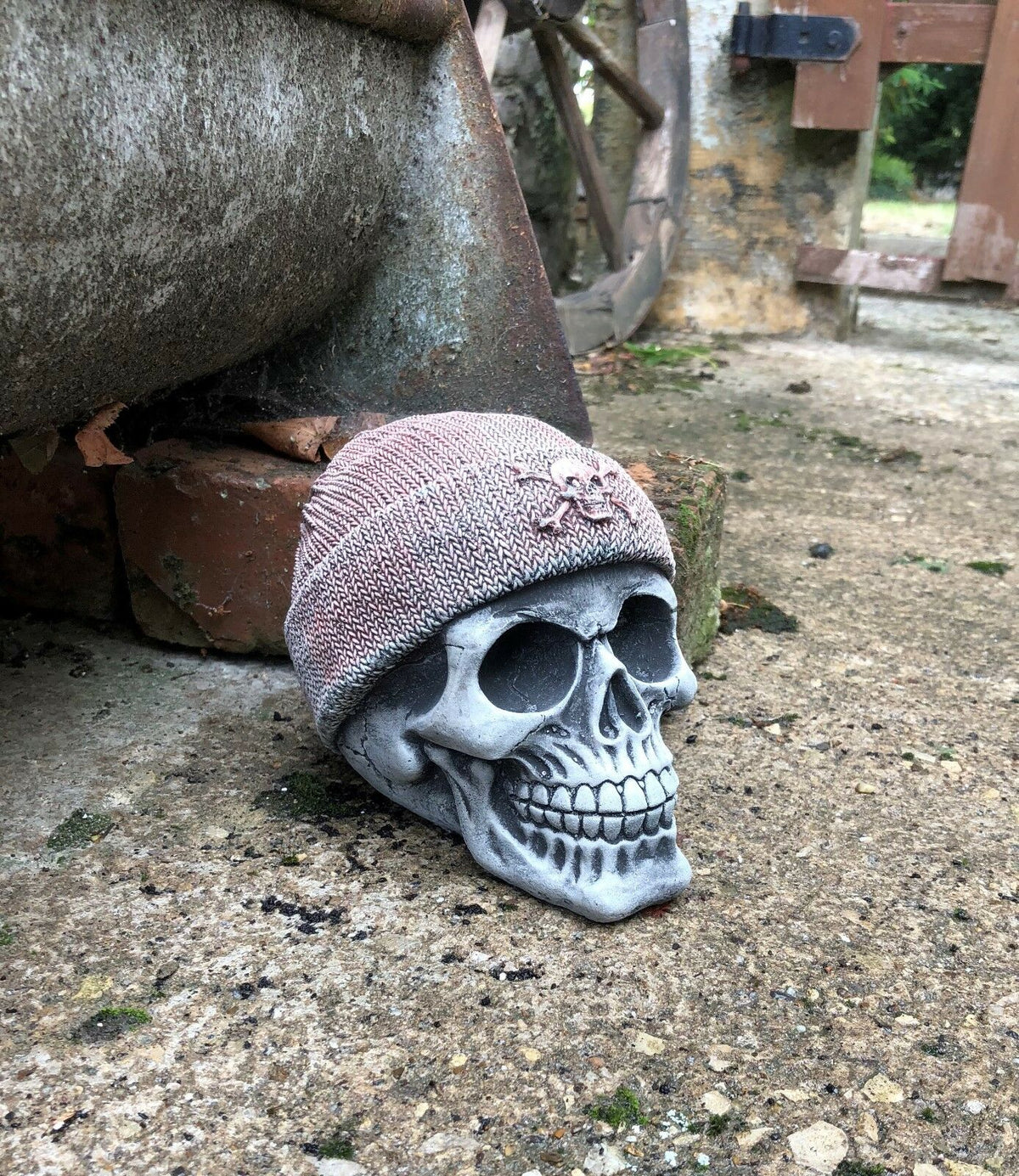 Side view of Stone Skull Beanie Ornament placed on patio, showcasing realistic limestone texture and antique finish for outdoor garden decoration.