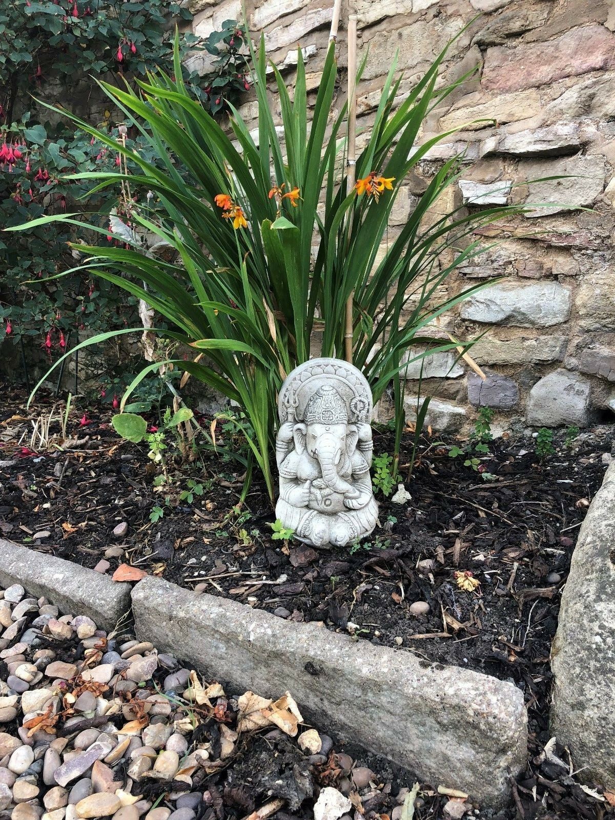 Ganesh Garden Ornament - Small Stone placed in a landscaped garden with stone border. Ideal for outdoor spiritual decor.