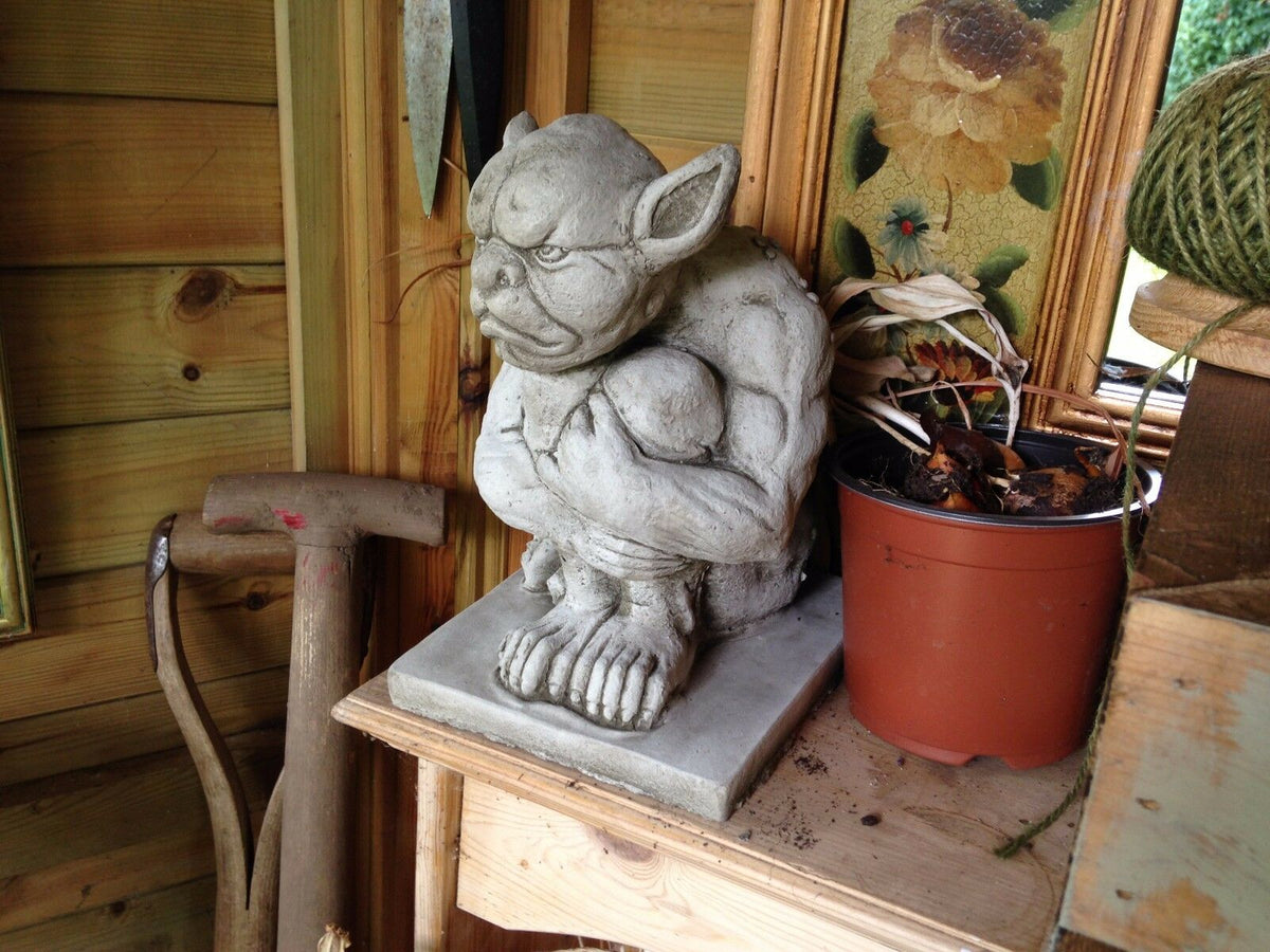 Side view of Grumpy Stone Gargoyle Statue on wooden shelf. Weatherproof garden sculpture for indoor or outdoor gothic decor.
