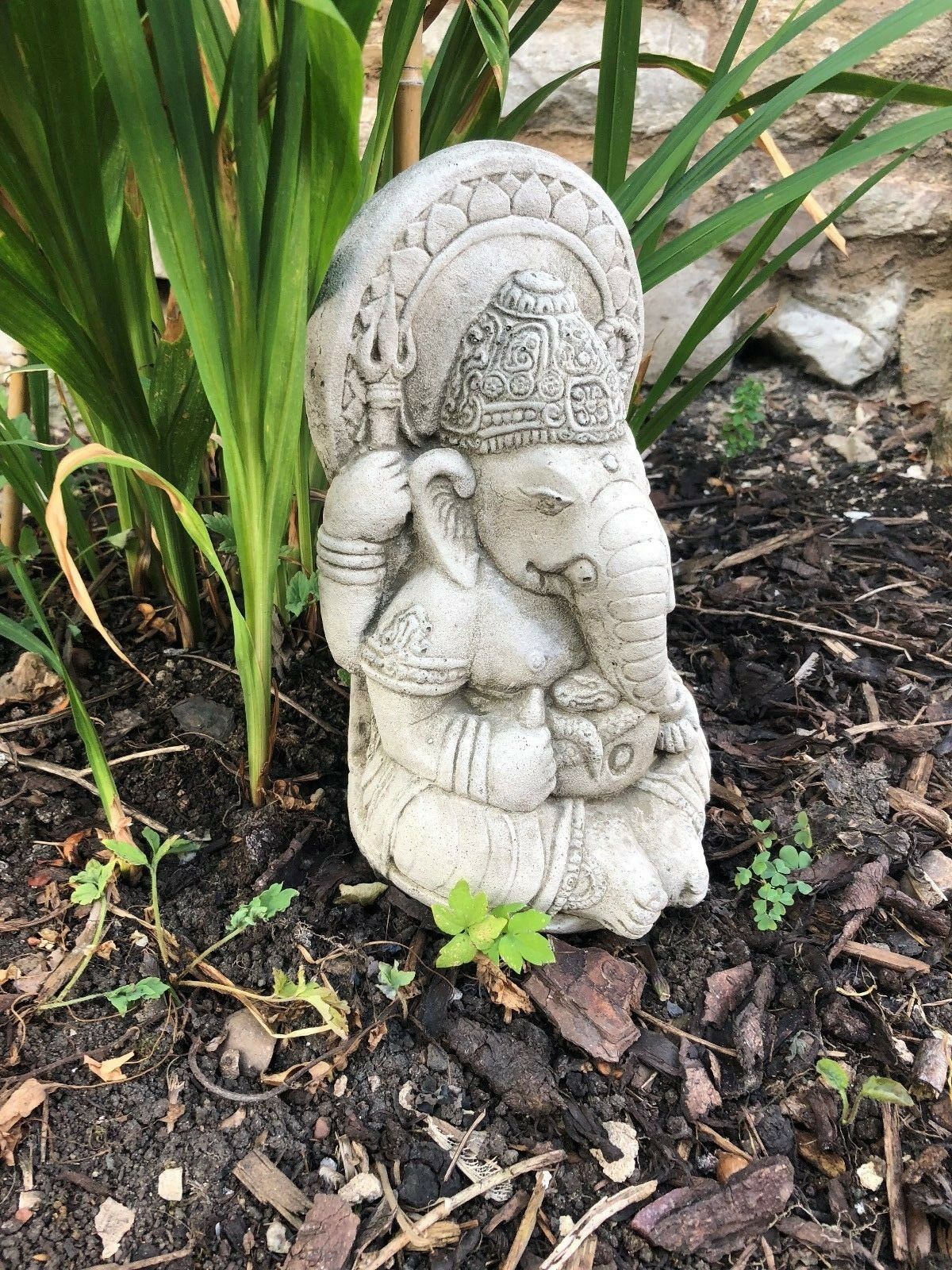 Side profile of Small Stone Ganesh Garden Ornament in mulch. Weatherproof and handmade for garden or patio use.