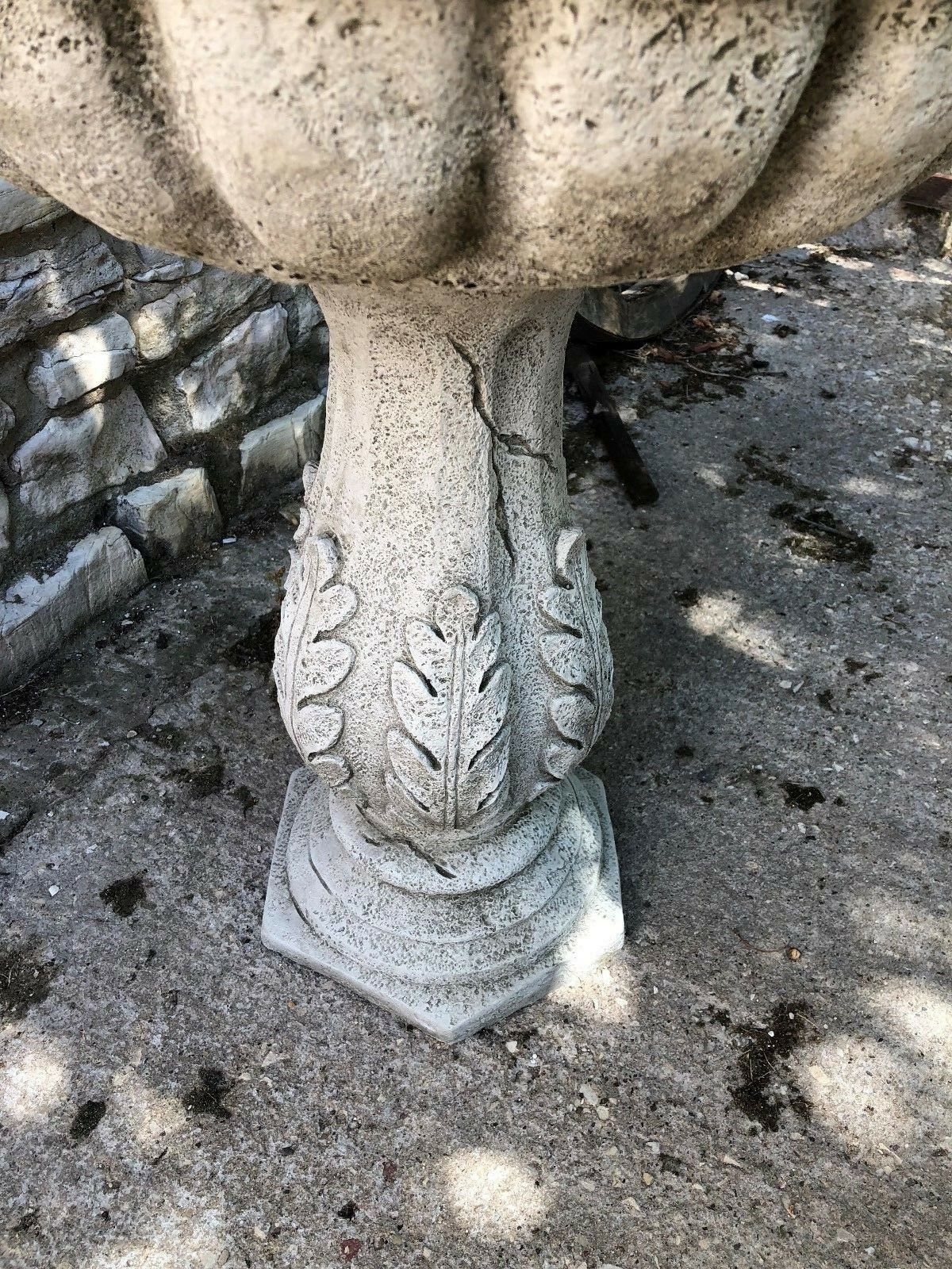 Close-up of leaf-engraved pedestal on antique stone garden bird bath, showcasing detailed craftsmanship and aged texture.