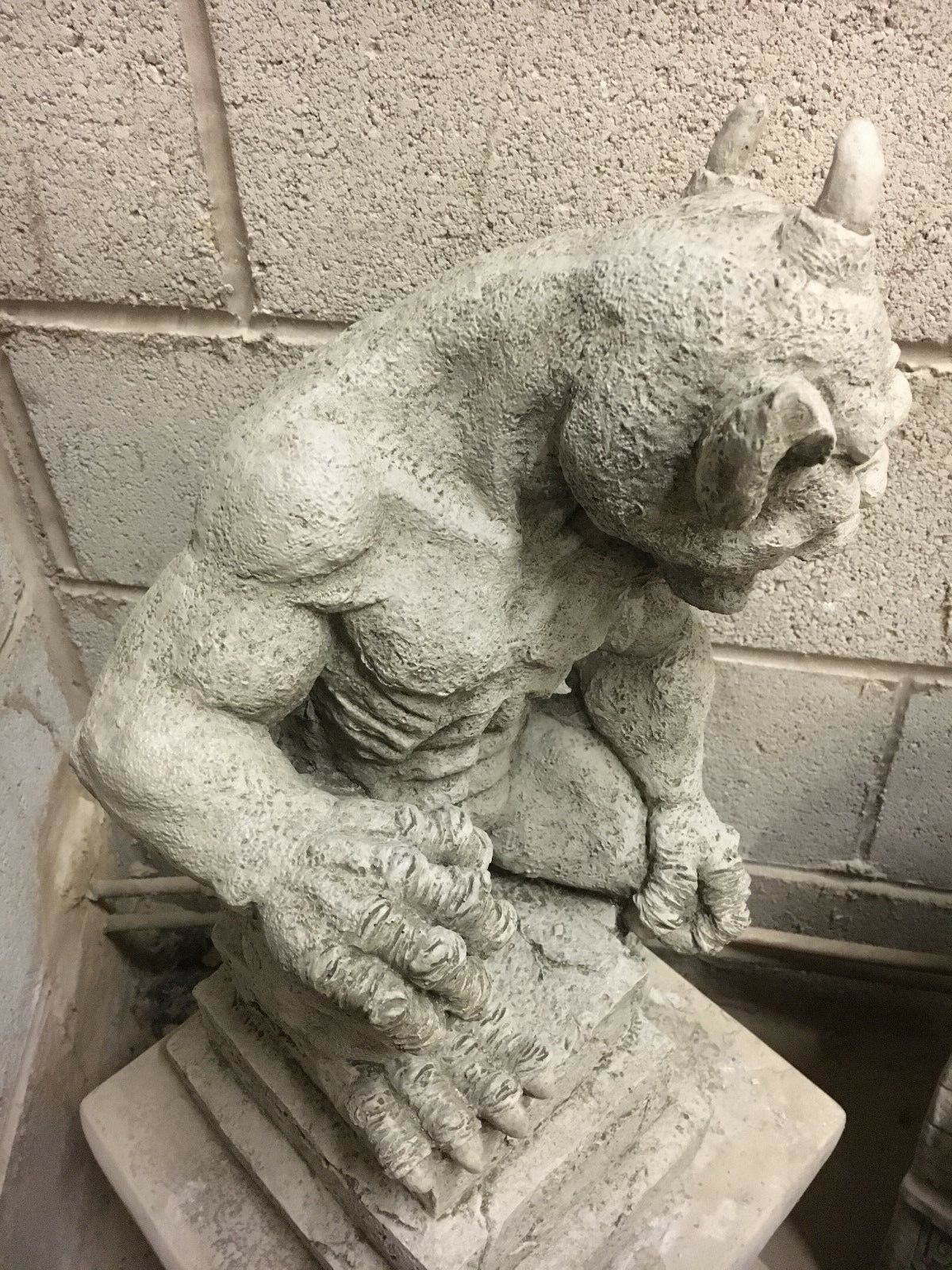 Close-up of stone gargoyle statue's fierce face with horned head and snarling expression, a striking garden sculpture centerpiece.