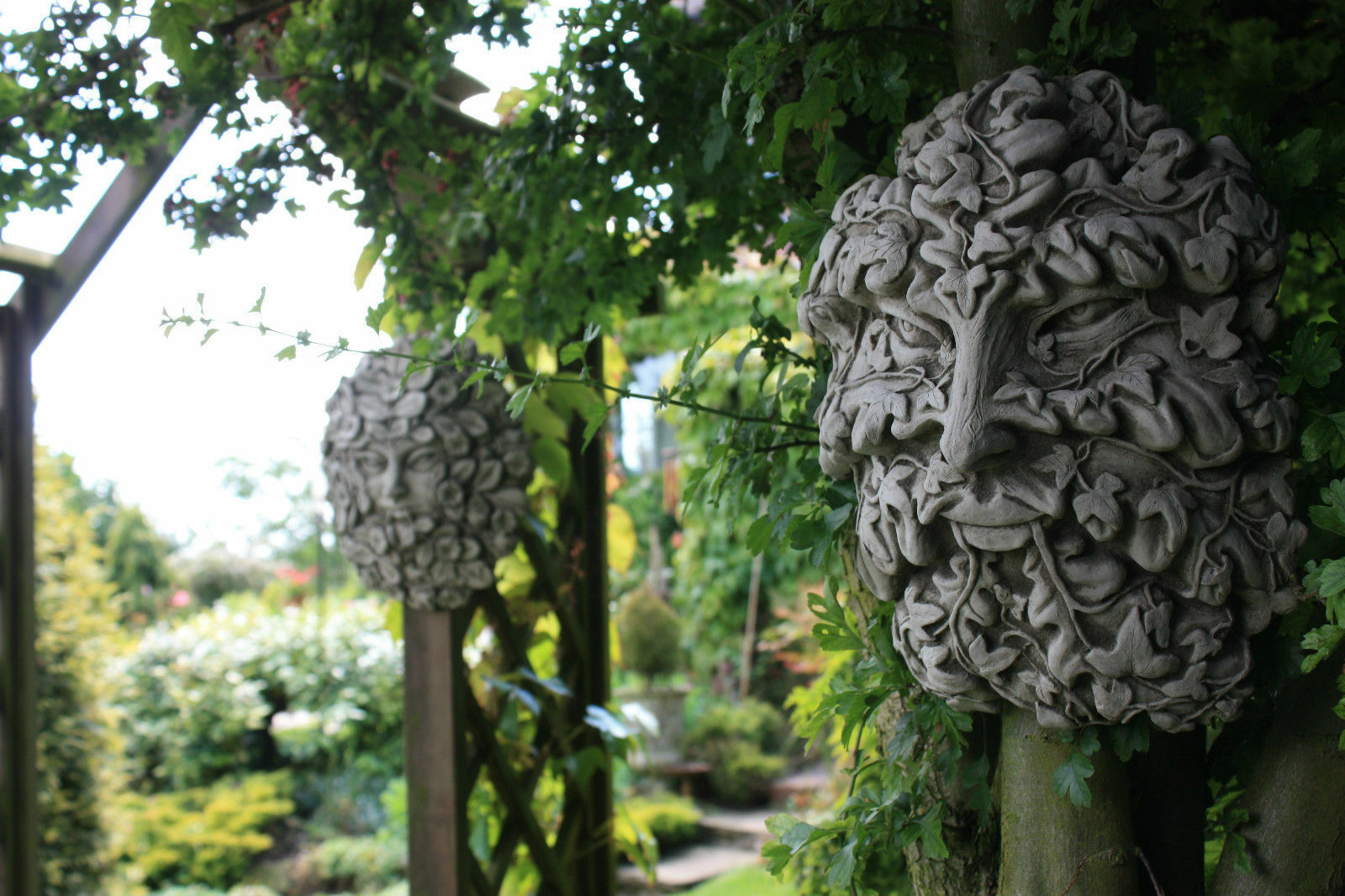 Pair of Greenman & Greenwoman garden wall plaques in solid stone finish, enhancing a wooden trellis with mythical charm.