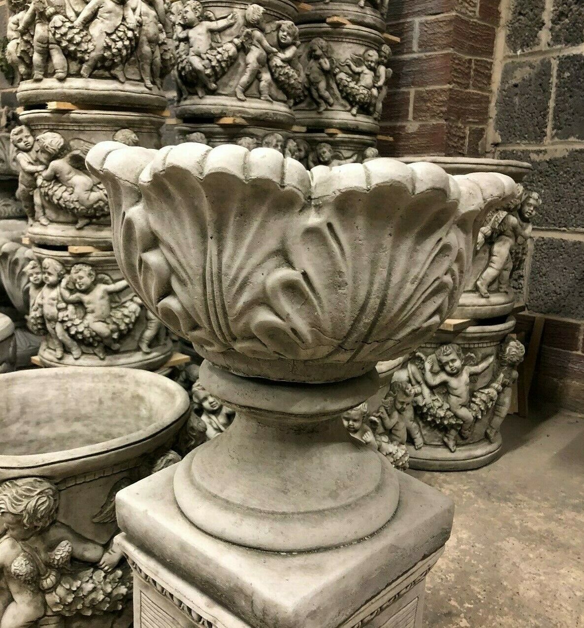 Handcrafted Small Tulip Garden Planter in antique limestone finish, surrounded by ornate garden urns and statues.