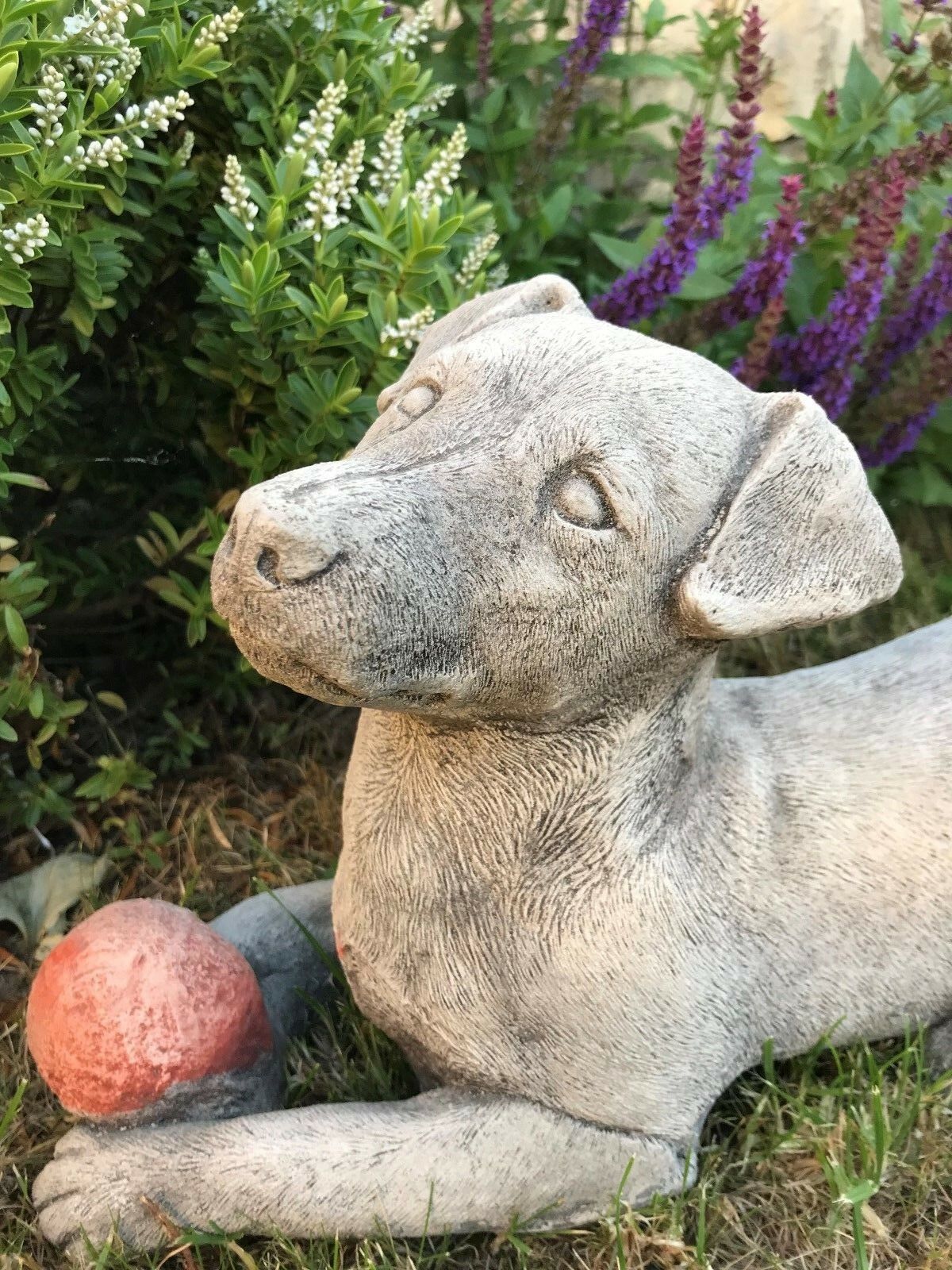 Close-up of Jack Russell Dog Garden Ornament with detailed stone texture and red ball, surrounded by vibrant greenery and flowers.