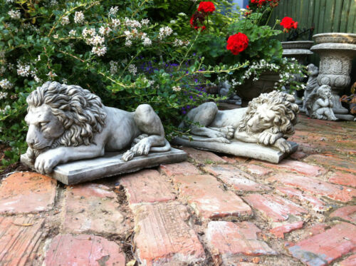 Stone lion garden statues resting on brick patio surrounded by red and white flowers. Elegant decor for outdoor spaces with free UK delivery.