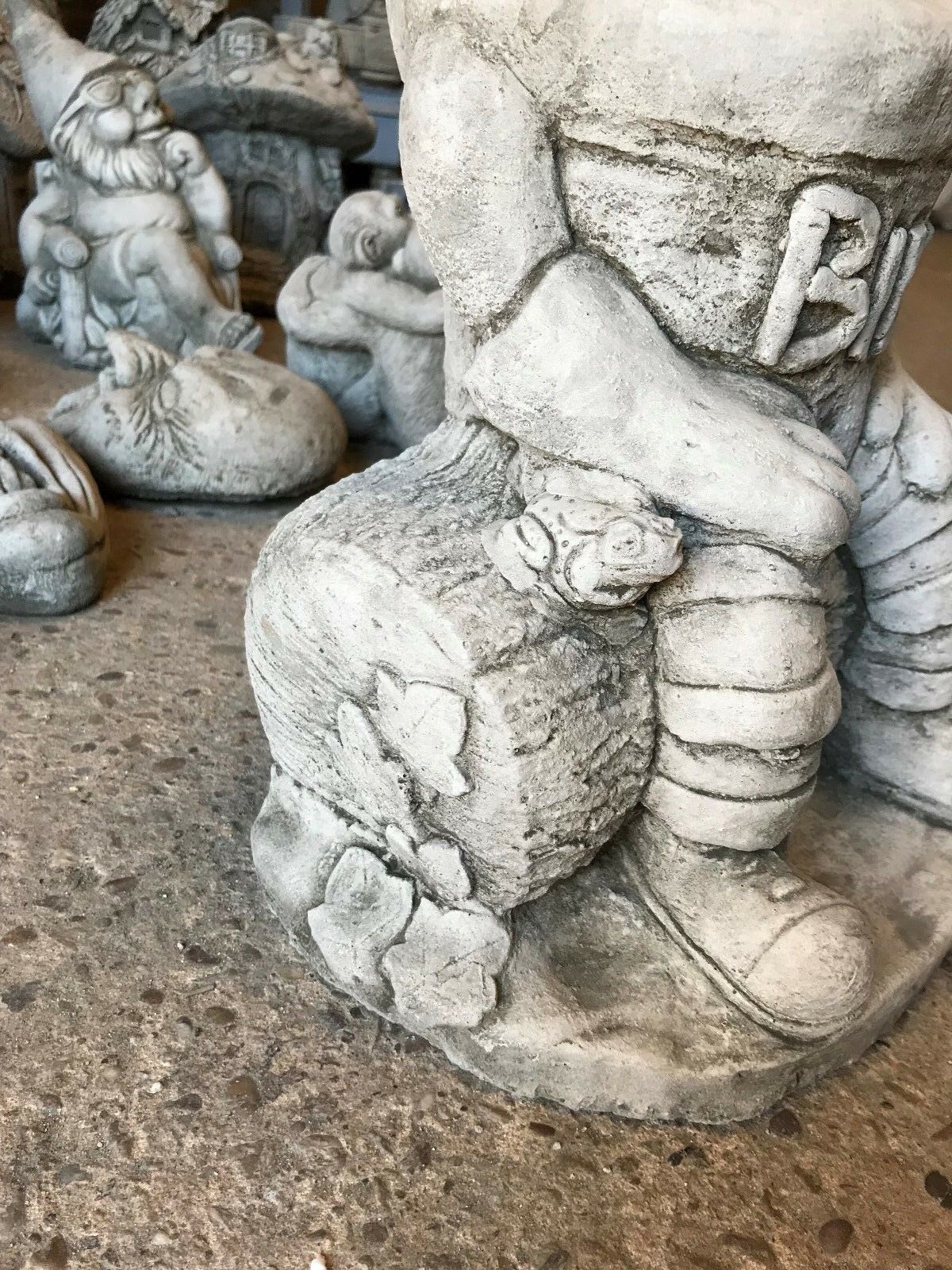 Detail of the Stone Bill statue's base, showing carved log texture with ivy and a small frog, enhancing its rustic garden appeal.