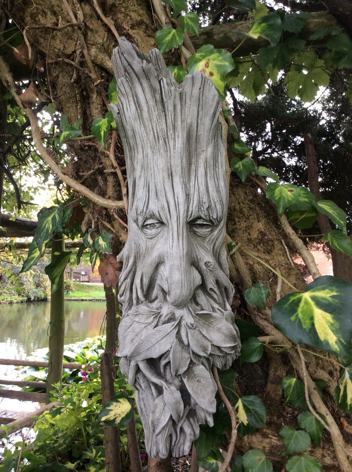 Durable Greenman garden plaque hanging on a tree trunk, crafted from stone leaf with mythological face and leaf beard.