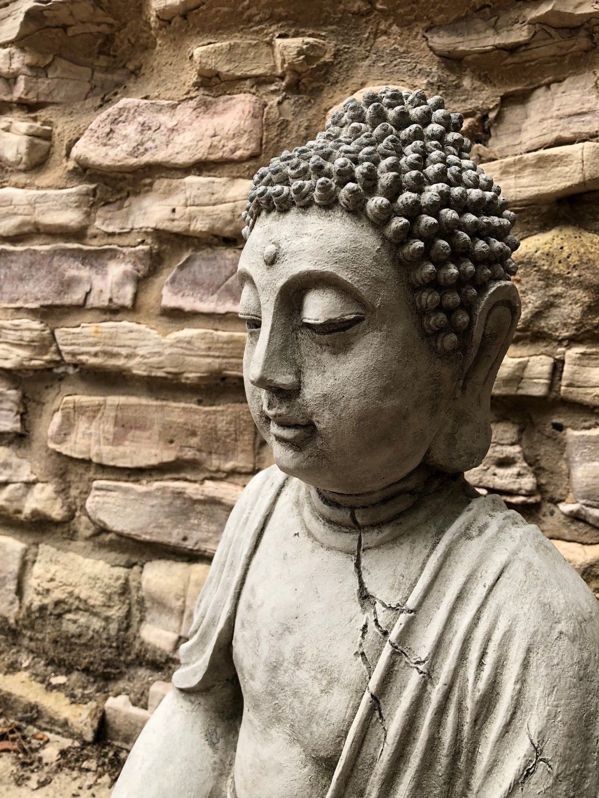 Close-up of Buddha Statue's serene face and textured hair, highlighting antique stone finish and meditative expression for garden ambiance.