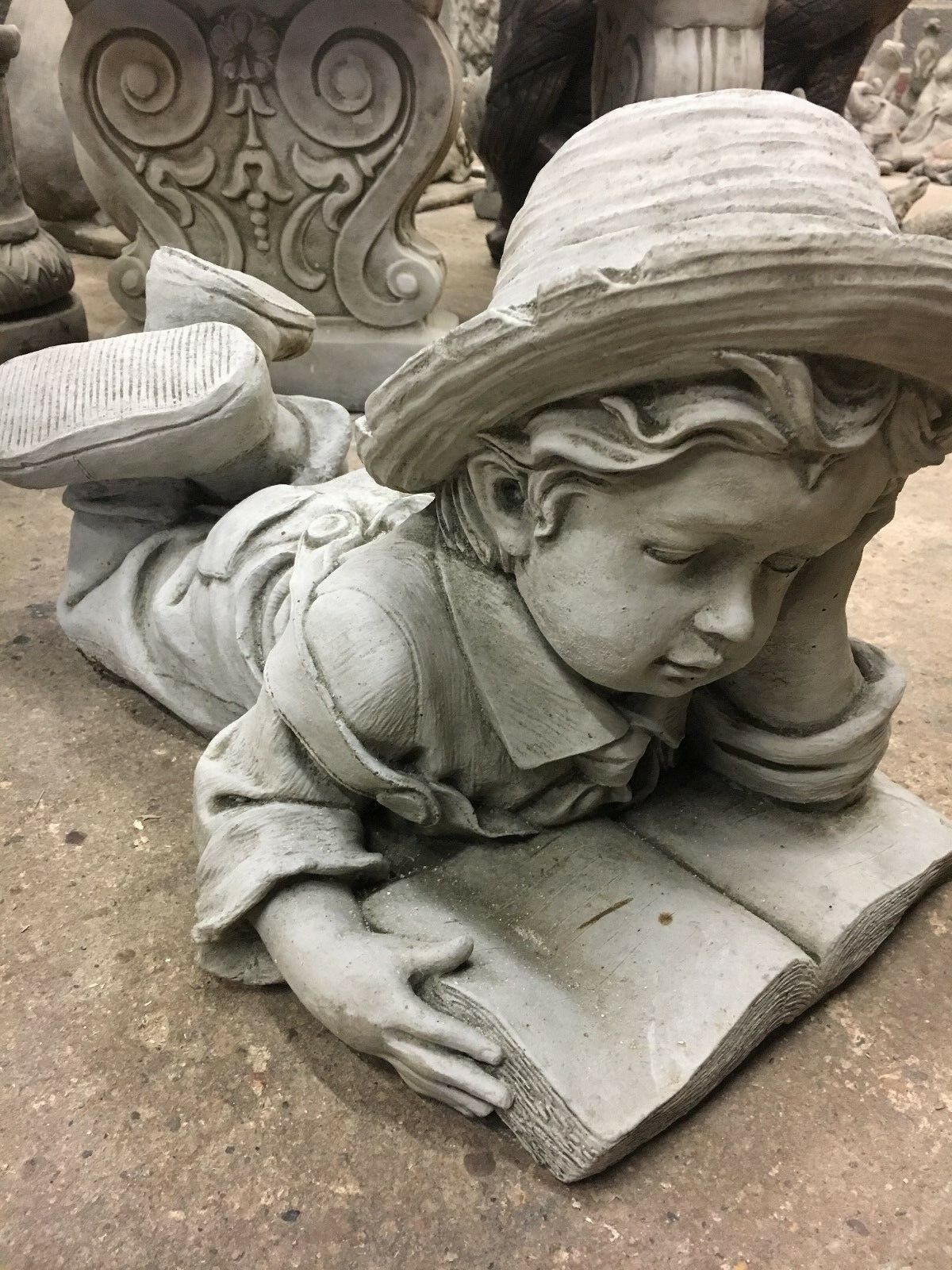 Close-up of stone Reading Boy Statue with hat and book, showcasing fine limestone craftsmanship for garden ornament use.