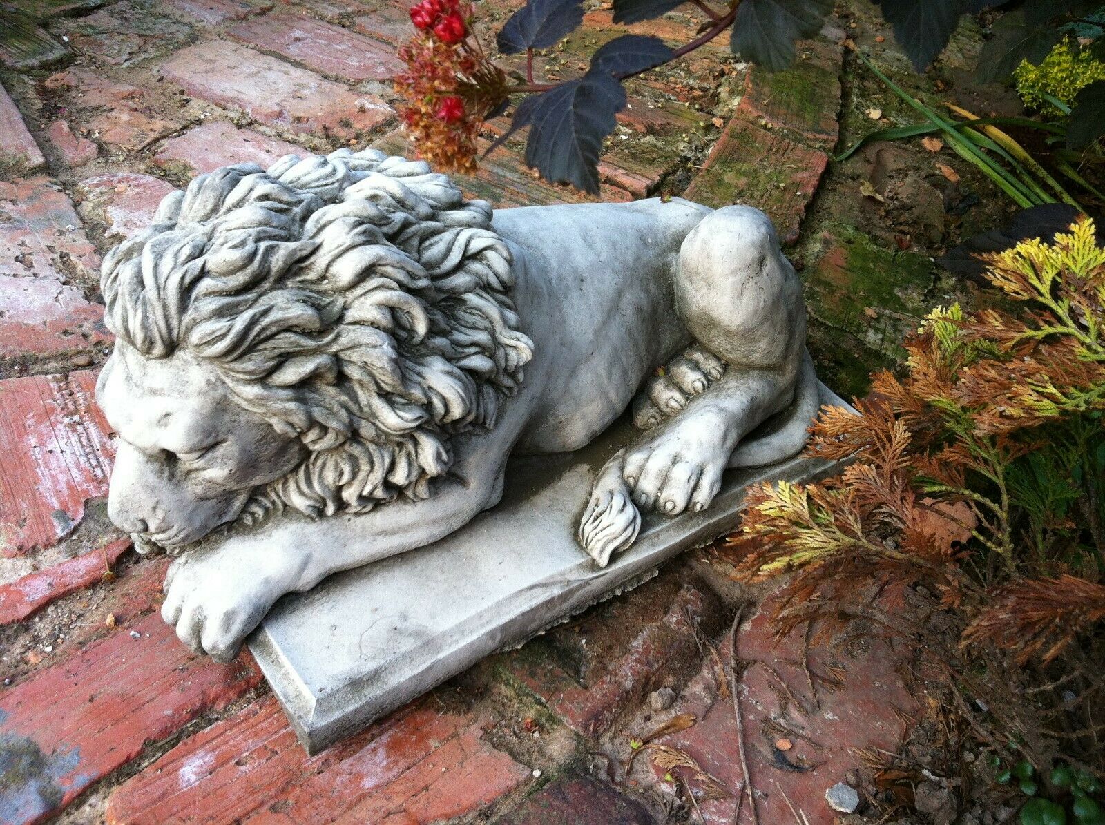 Close-up of a reclining stone lion statue on a rustic brick path, ideal for timeless garden decor and weather-resistant outdoor ornamentation.