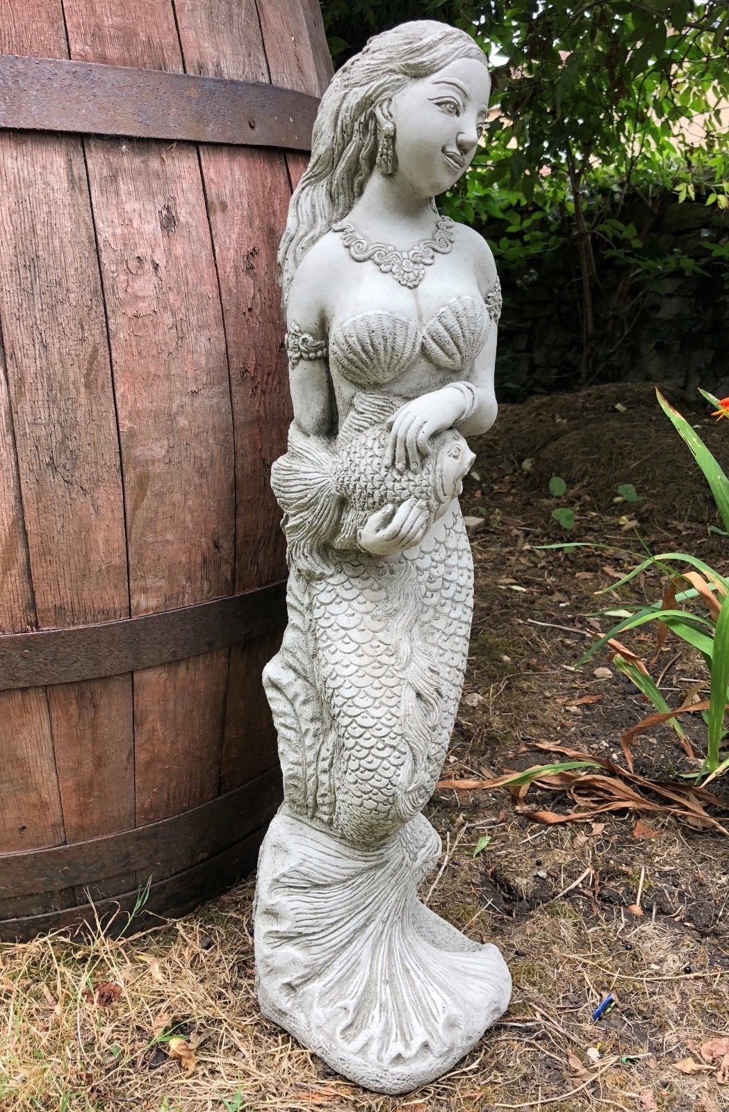 Detailed stone mermaid statue holding a fish, designed as a water spout feature for garden ponds or outdoor decorative use.