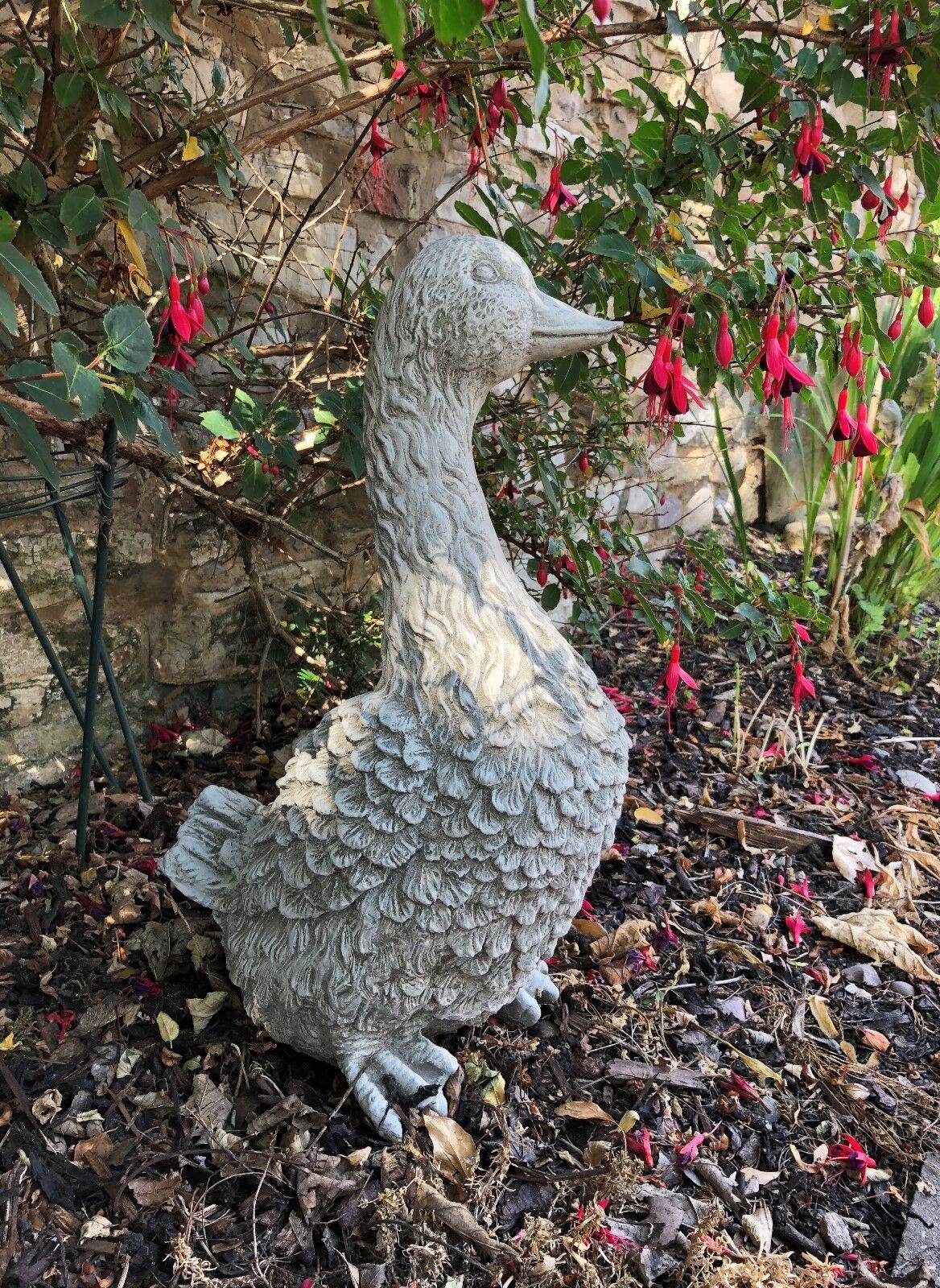 Goose Garden Statue - Stone Goose Decor standing near a stone wall and flower bed. Adds rustic charm to any garden or yard space.