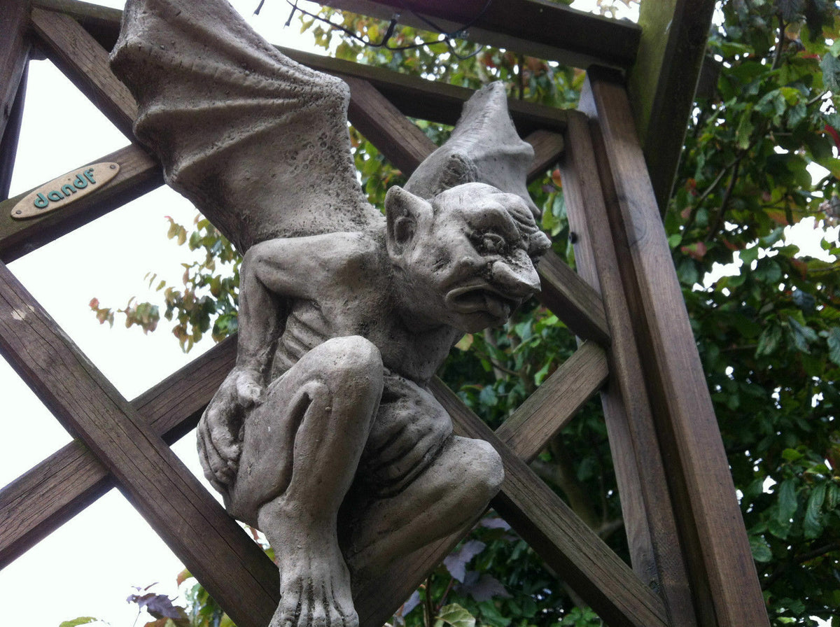 Stunning Stone Winged Gargoyle Sculpture Garden Ornament perched on wooden trellis, showcasing detailed wings and fierce expression for outdoor decor.