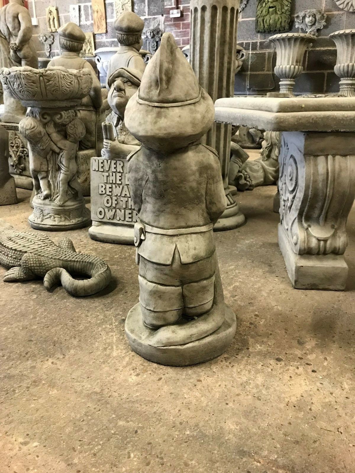 Rear view of antique grey fireman garden statue, highlighting sculpted belt and helmet, perfect for weather-resistant outdoor decor.