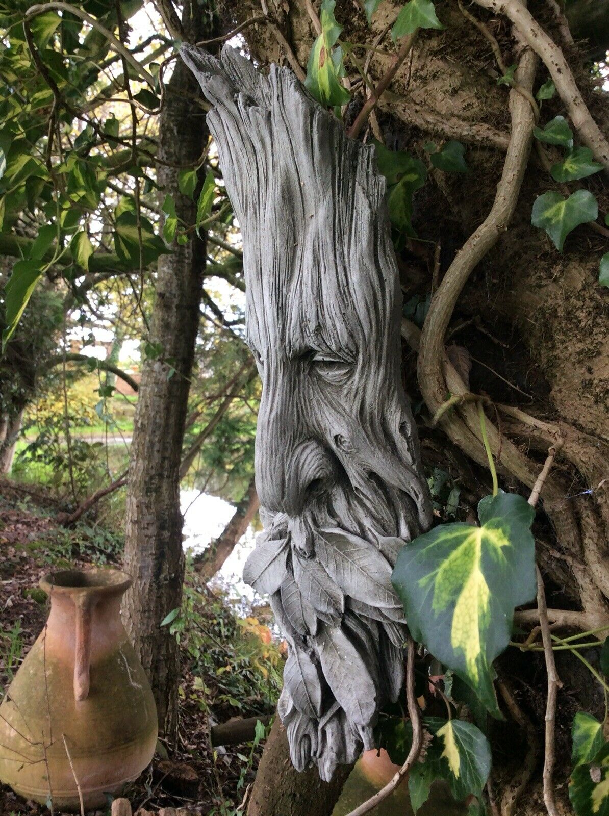 Side view of Stone Leaf Greenman Plaque showing detailed carving and natural integration with garden vines and tree bark.