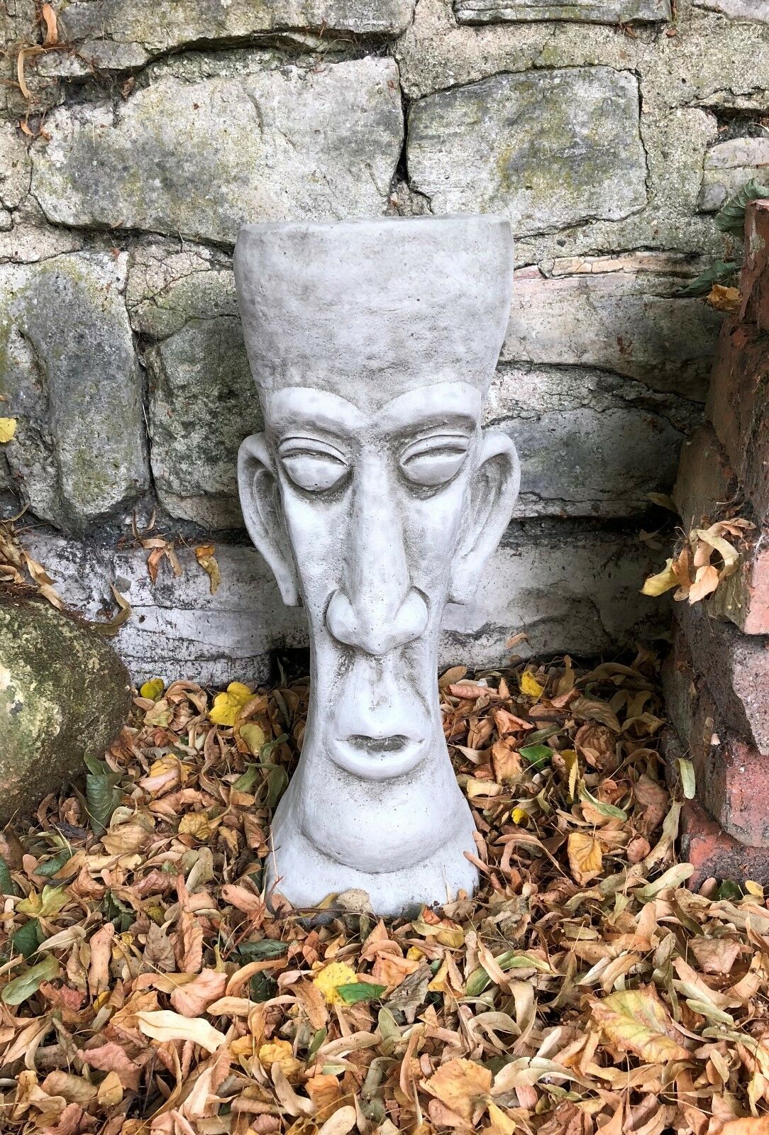 Stone Easter Island Head Planter with antique grey finish placed in a garden setting, ideal for unique outdoor decor and plant display.