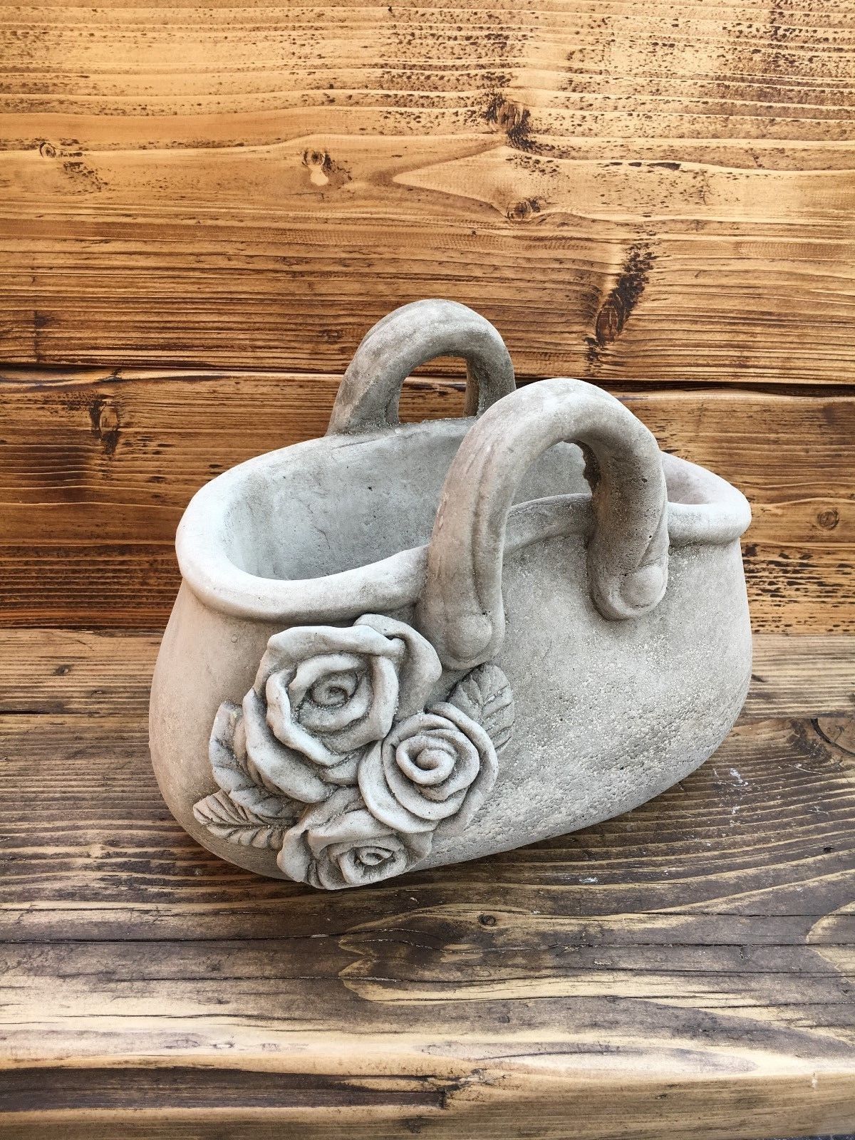 Front view of stone handbag planter with dual handles and rose design. Handmade from limestone for a rustic garden look.