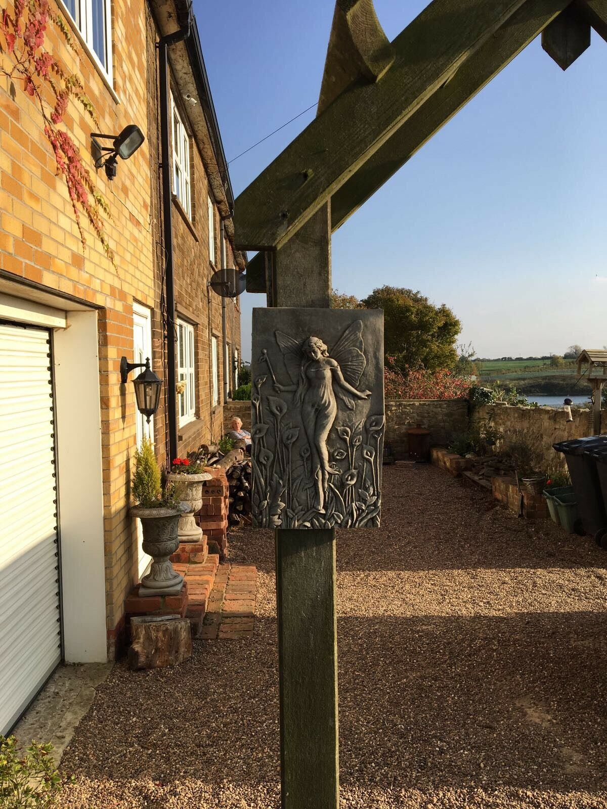 Fairy Garden Wall Plaque displayed on garden post near brick house, blending magical stone design with rustic outdoor setting.