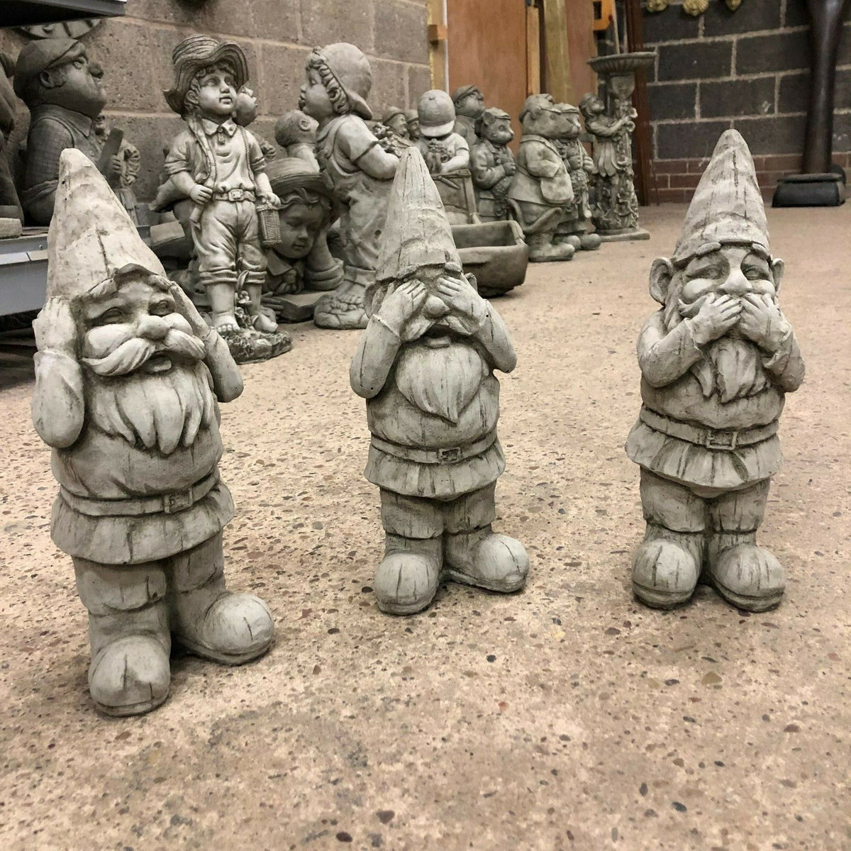 Gnome Statues Set - Stone Hear See Speak No Evil trio displayed on workshop floor. Ideal for whimsical garden decor and outdoor ornamentation.