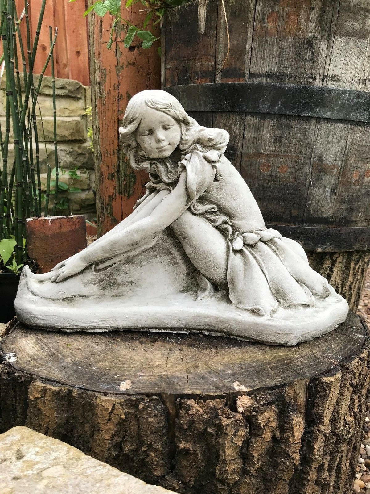 Stone Fairy Garden Ornament sculpture of a kneeling fairy girl with detailed dress, displayed on a tree stump in a rustic garden setting.