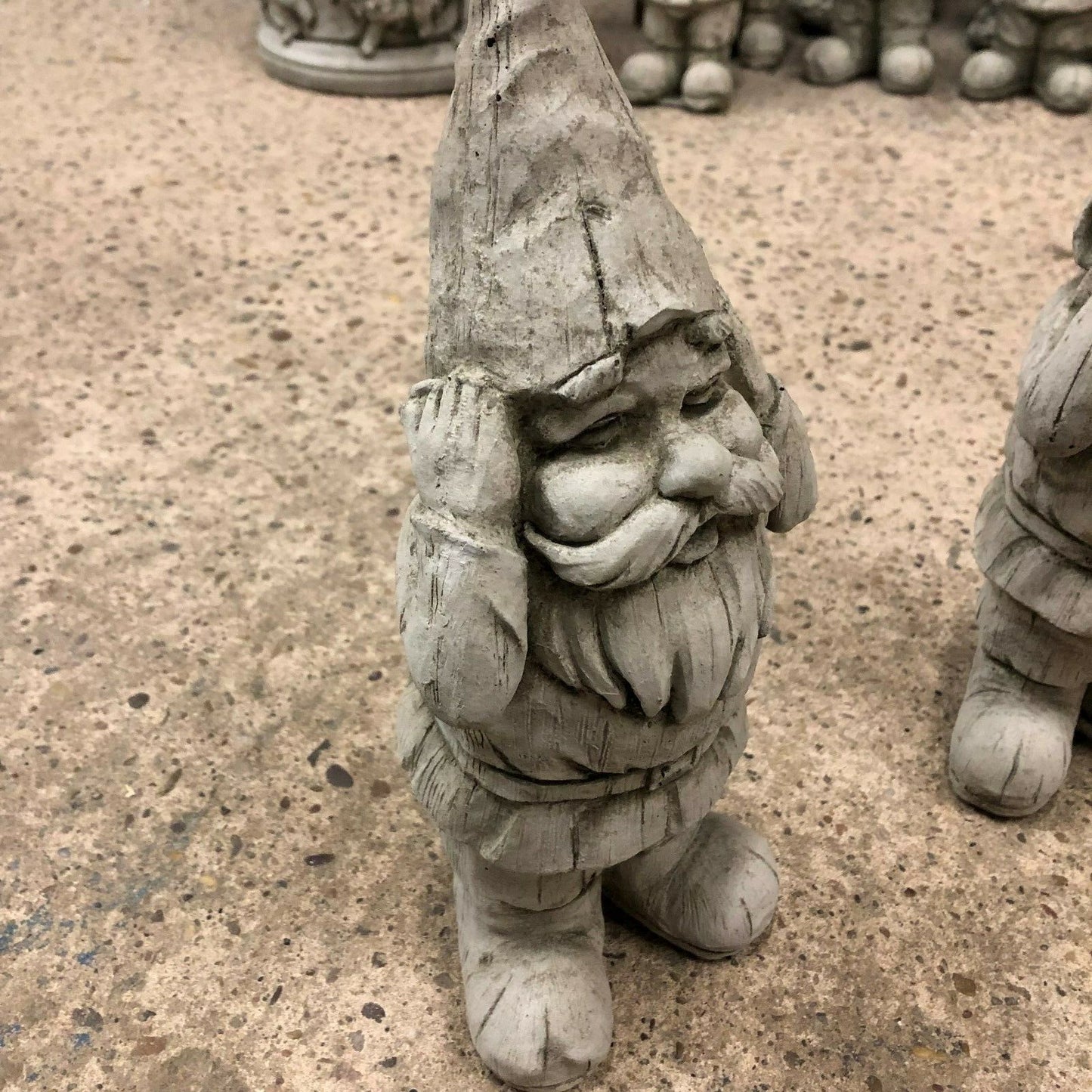 Close-up of 'Hear No Evil' stone gnome statue with hands on ears. Part of a charming garden decor trio for outdoor spaces.