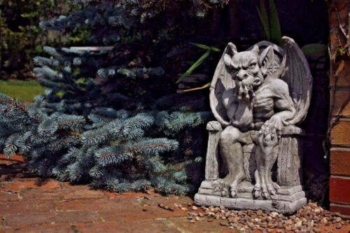 King Gargoyle Stone Statue - Weather Resistant Garden Art placed near pine tree and brick wall, perfect for mythical and gothic garden styling.