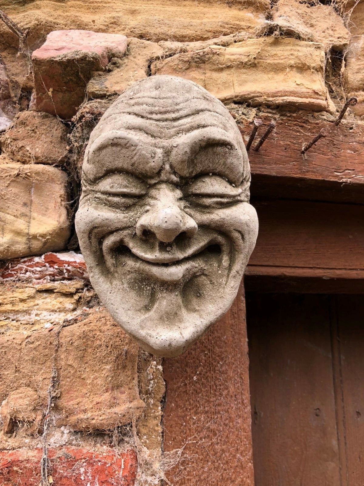 Smug Smile Stone Plaque mounted on rustic brick wall, ideal for outdoor garden decor. Durable limestone with antique grey finish adds character.