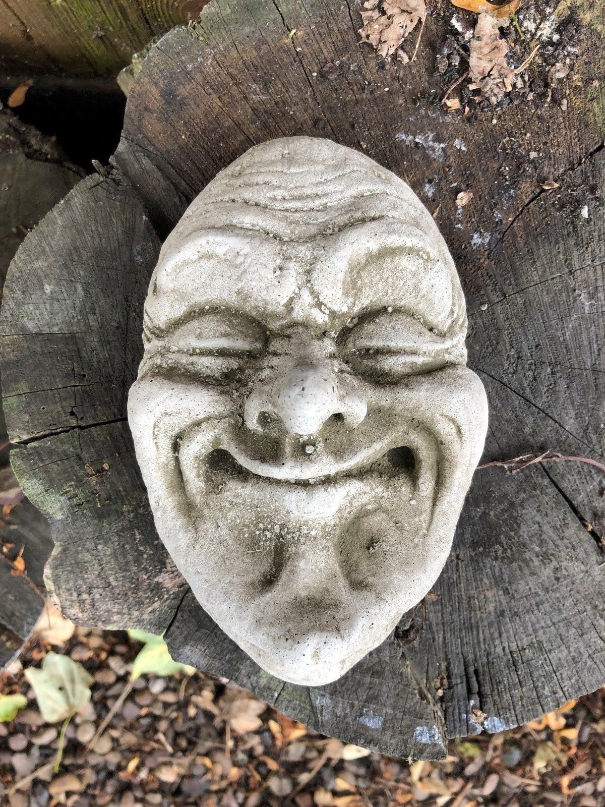 Smug Smile Stone Plaque resting on tree stump, showcasing detailed facial features. Perfect garden ornament for whimsical outdoor decoration.