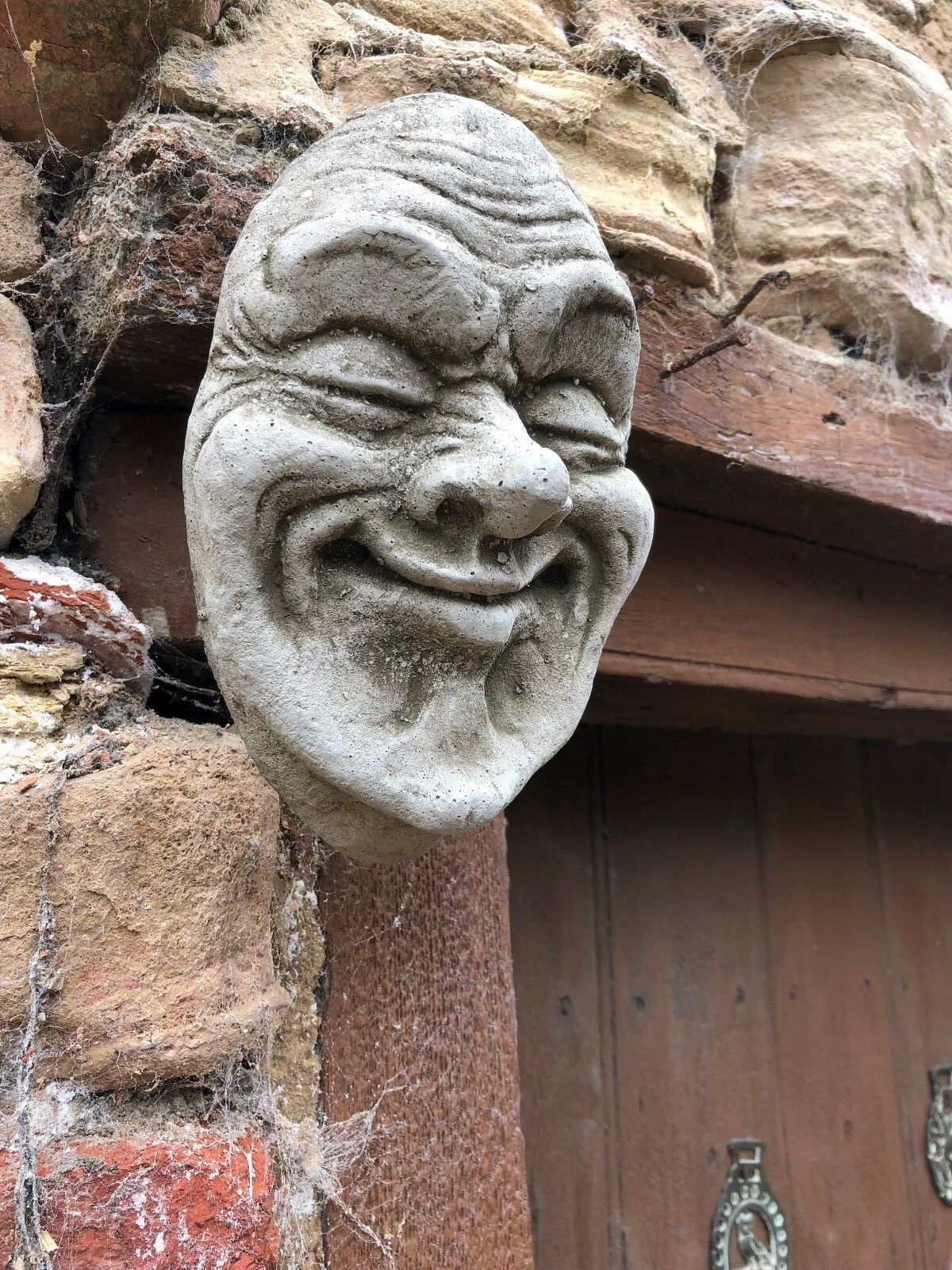 Side view of Smug Smile Stone Plaque on weathered wall, highlighting its 3D sculpted design. Waterproof and durable for garden use.