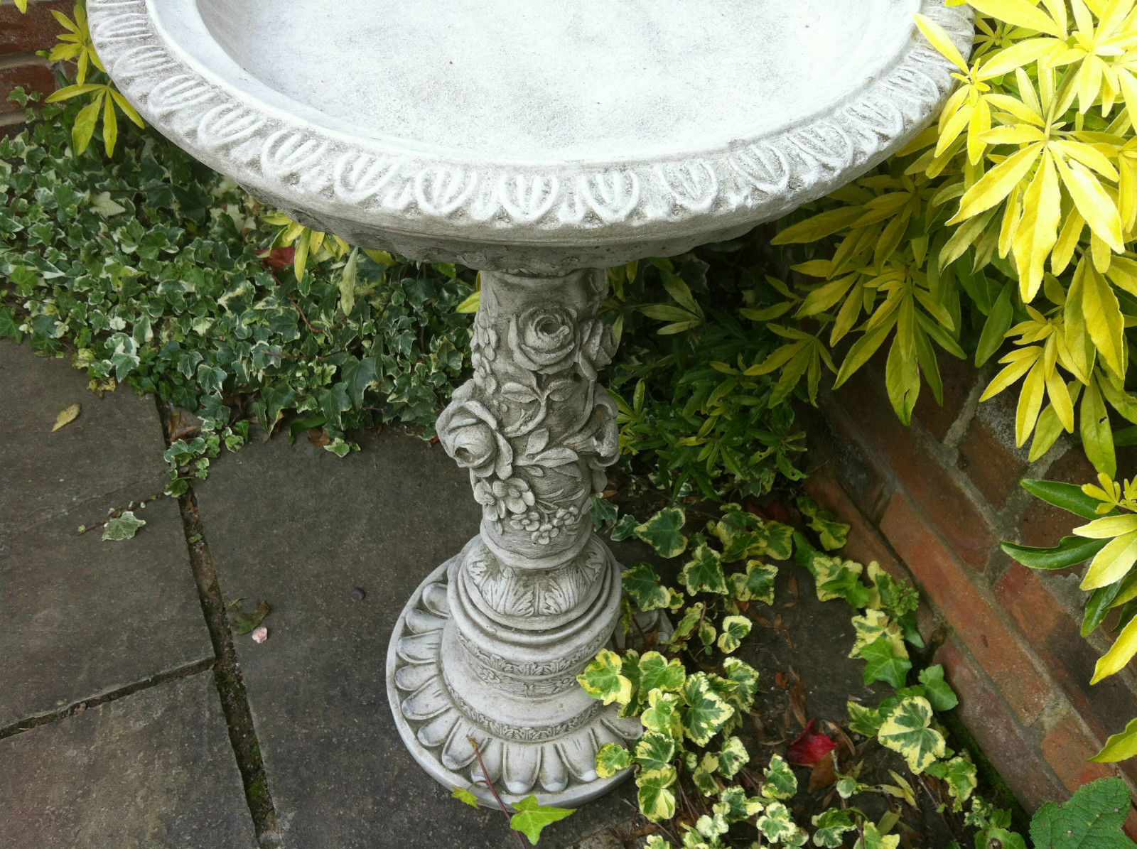 Detailed view of the bird bath's ornate bowl and floral stem. Durable limestone with antique finish perfect for garden decor.