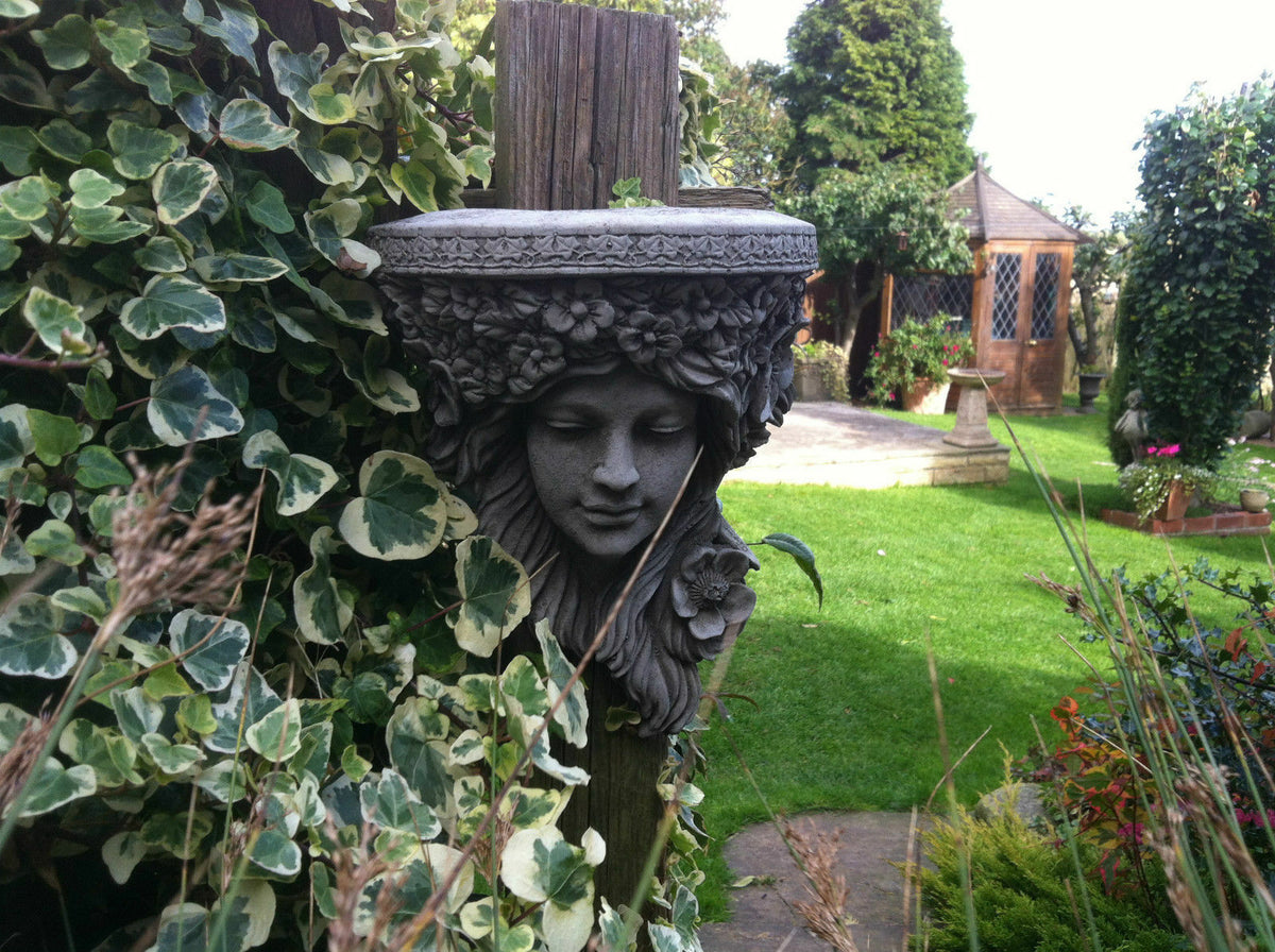 Garden Wall Shelf - Lady Stone Plaque mounted on a wooden post surrounded by green ivy in a landscaped backyard. Ideal for outdoor wall decor.