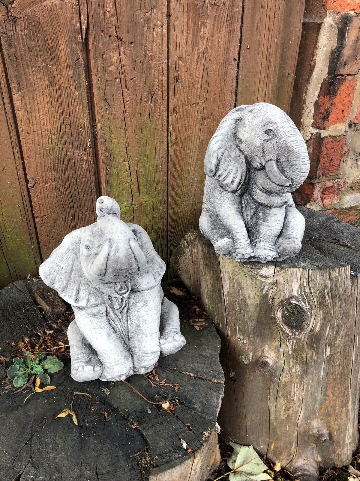 Pair of stone baby elephant sculptures with detailed textures, ideal for garden decoration or lawn ornamentation in natural settings.