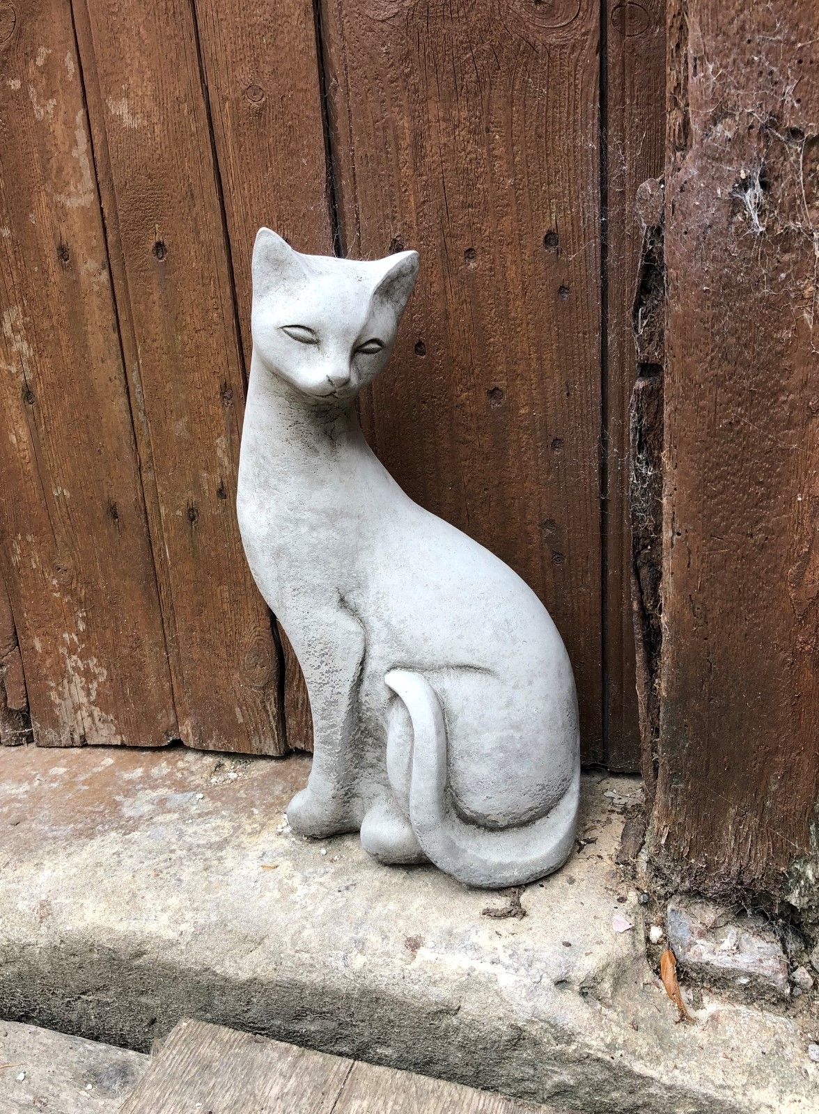 Single stone Siamese cat statue resting against a wooden wall, showcasing its sleek design for garden or porch display.