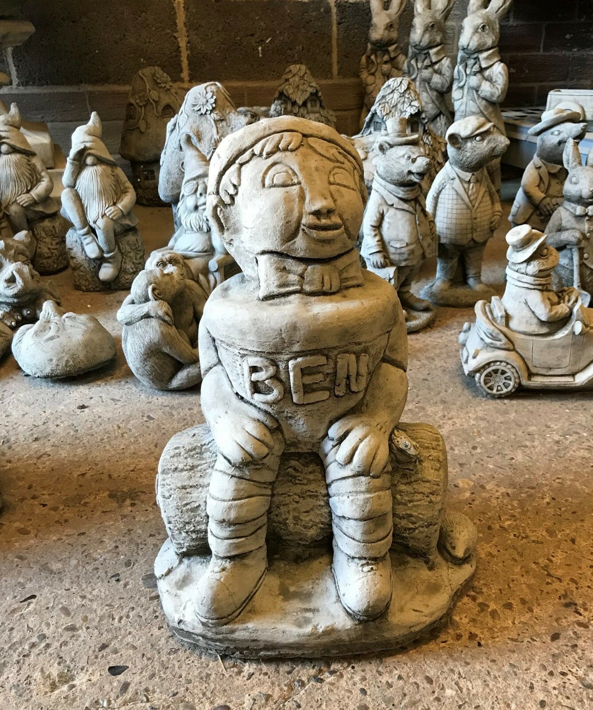 Stone Ben statue from the Garden Ornament Collection, seated on a log with antique finish, ideal for whimsical garden decor.