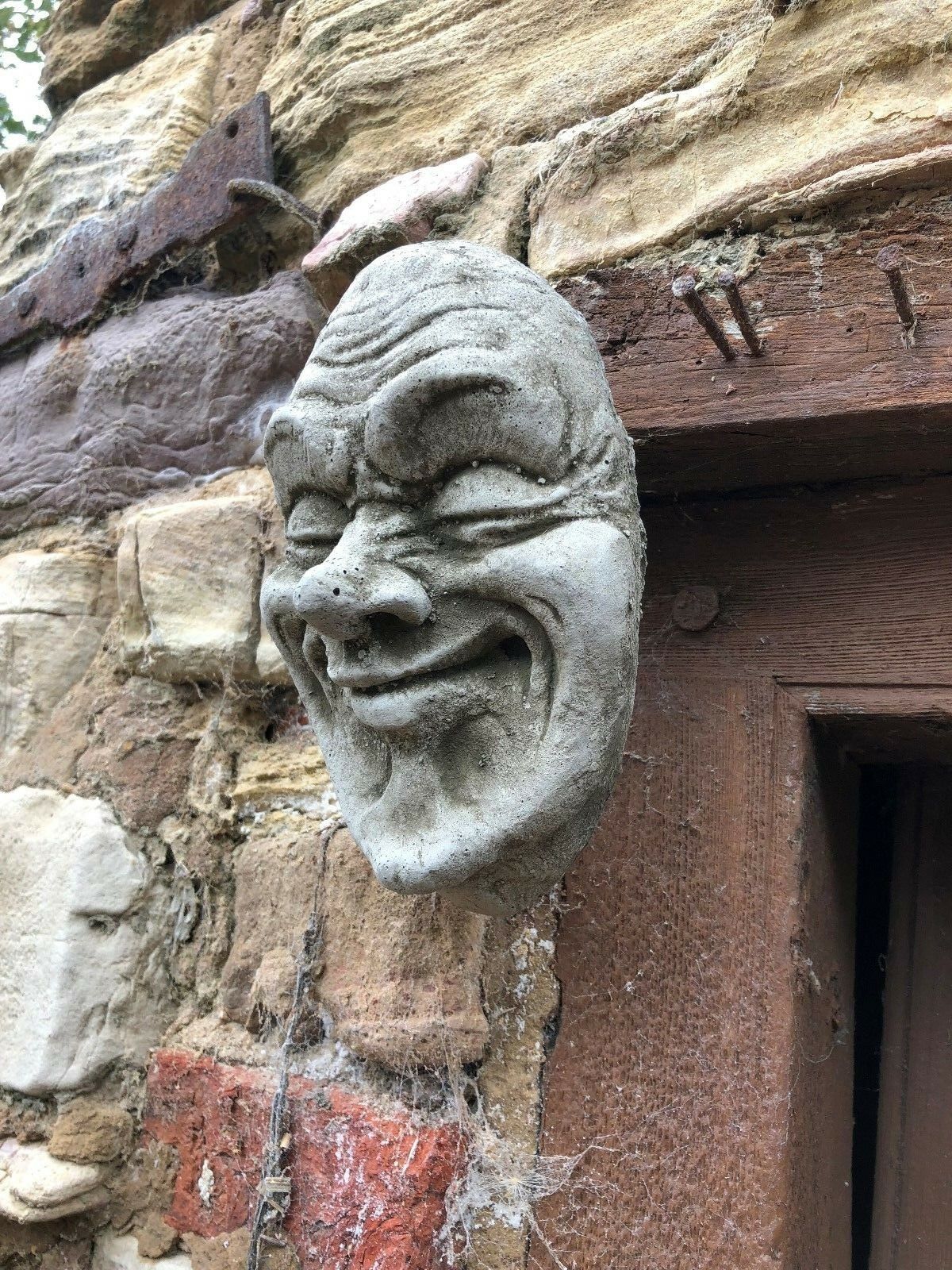 Angled view of Smug Smile Stone Plaque fixed to stone wall, showing textured limestone finish. Unique garden ornament for home decor.