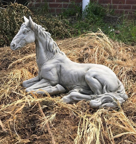 Stone Resting Horse Statue - Garden Ornament placed on dried grass, showcasing its elegant antique finish and realistic detailing.