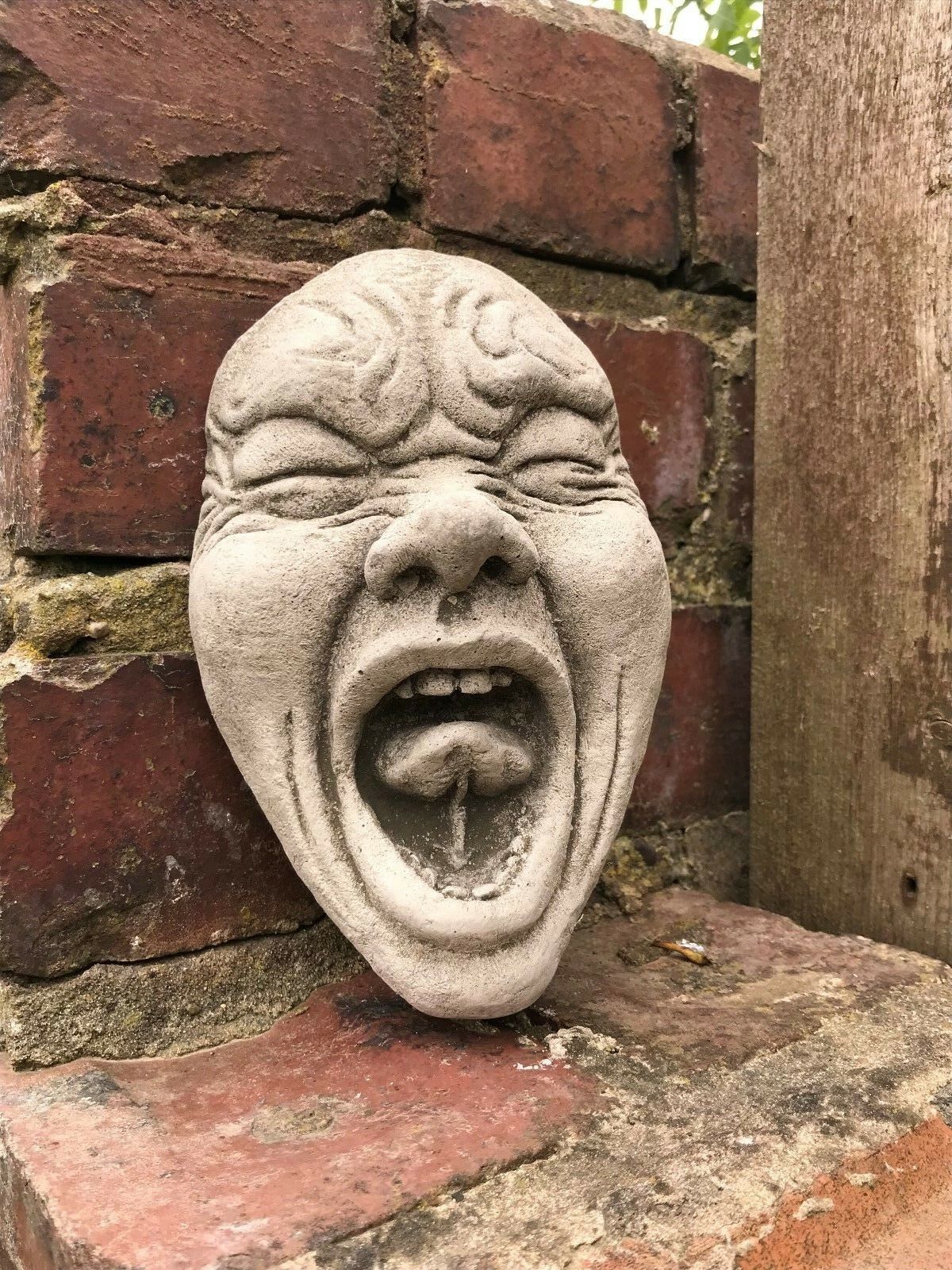 Funny Garden Wall Plaque - Stone Scream Face with exaggerated expression and antique grey finish, mounted on a brick wall for outdoor decor.