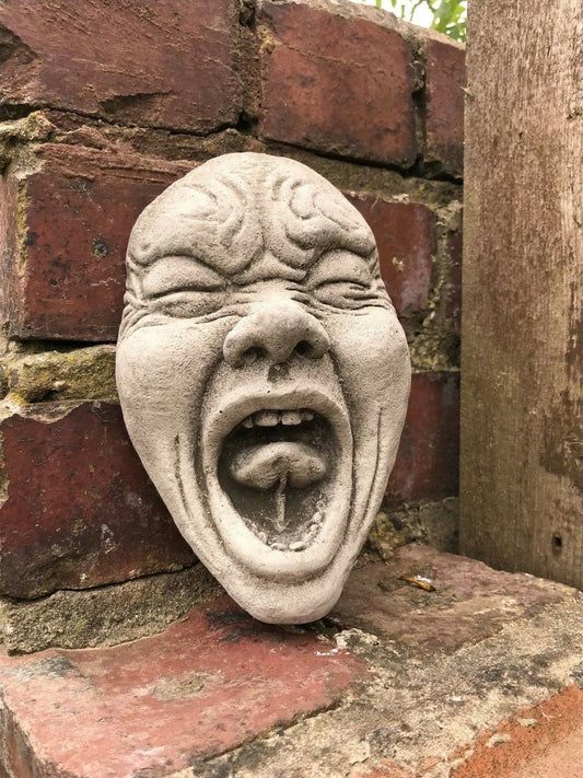 Funny Garden Wall Plaque - Stone Scream Face with exaggerated expression and antique grey finish, mounted on a brick wall for outdoor decor.