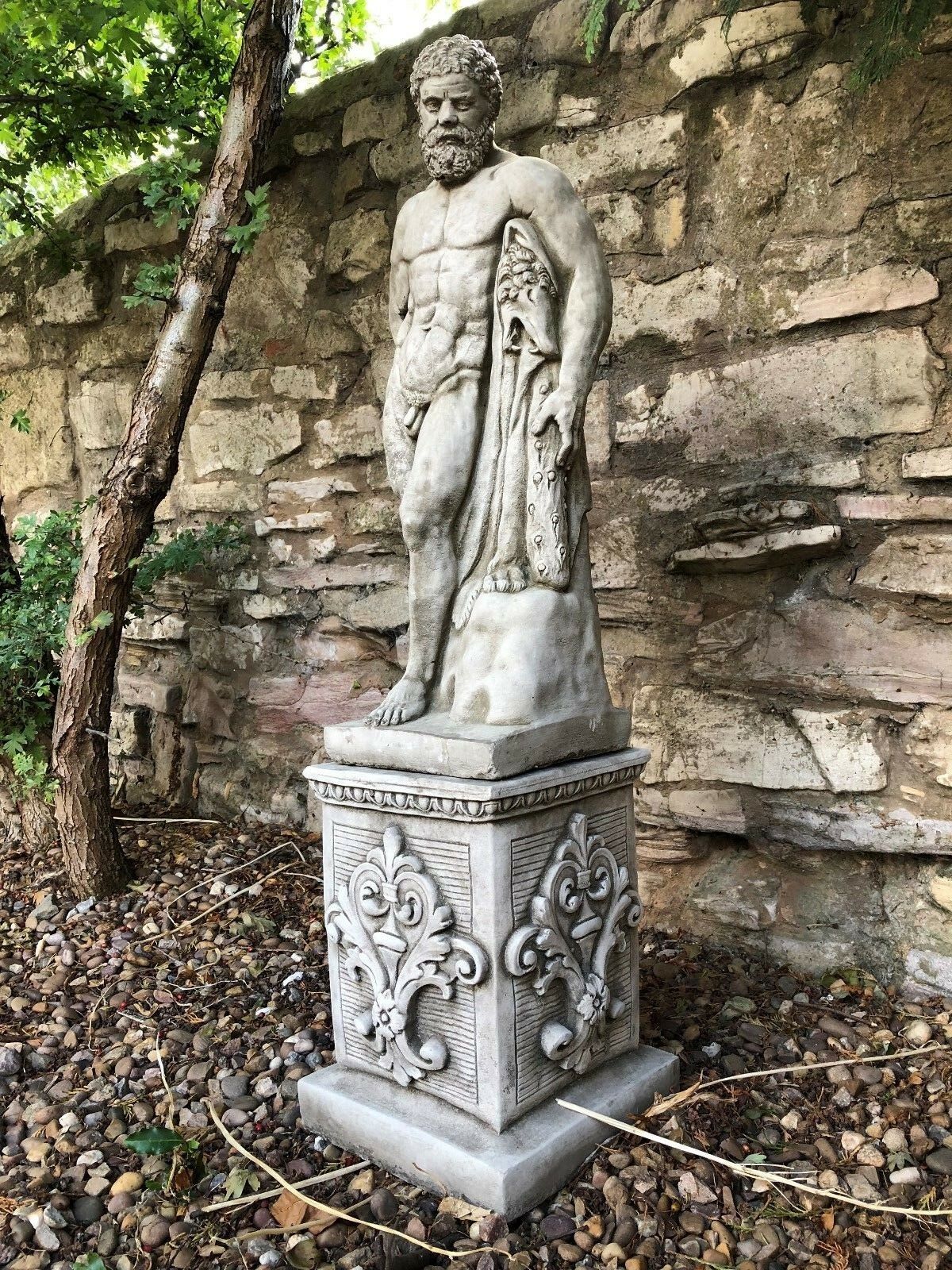 Angled side view of Hercules garden sculpture on limestone plinth, highlighting muscular detail and lion skin drape.