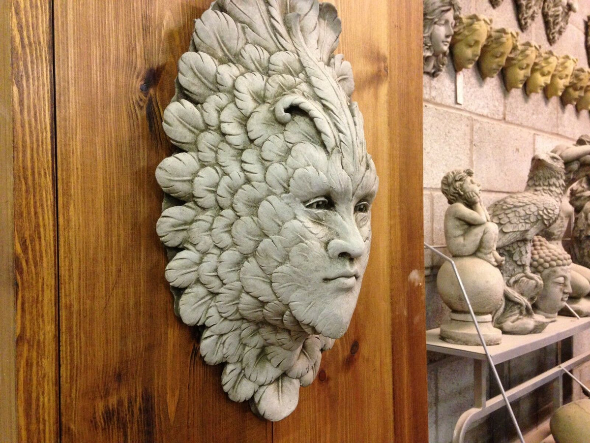 Greenman Garden Wall Plaque - Stone Feather Face hanging on indoor wooden wall. Handmade limestone ornament for home or garden decor.