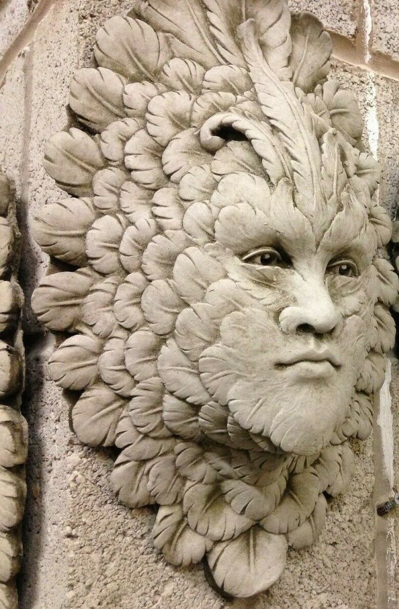 Detailed view of Stone Feather Greenman Wall Plaque on stone wall. Intricate leaf design in durable limestone for outdoor decoration.