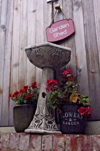 Stone Art Nouveau Bird Bath beside red geraniums and rustic decor near a garden shed. Freestanding and weather-resistant.