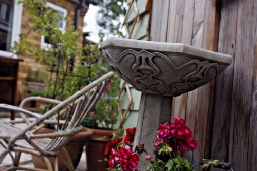 Side view of Art Nouveau Bird Bath with intricate carvings, surrounded by patio furniture and potted plants. Stylish garden accent.