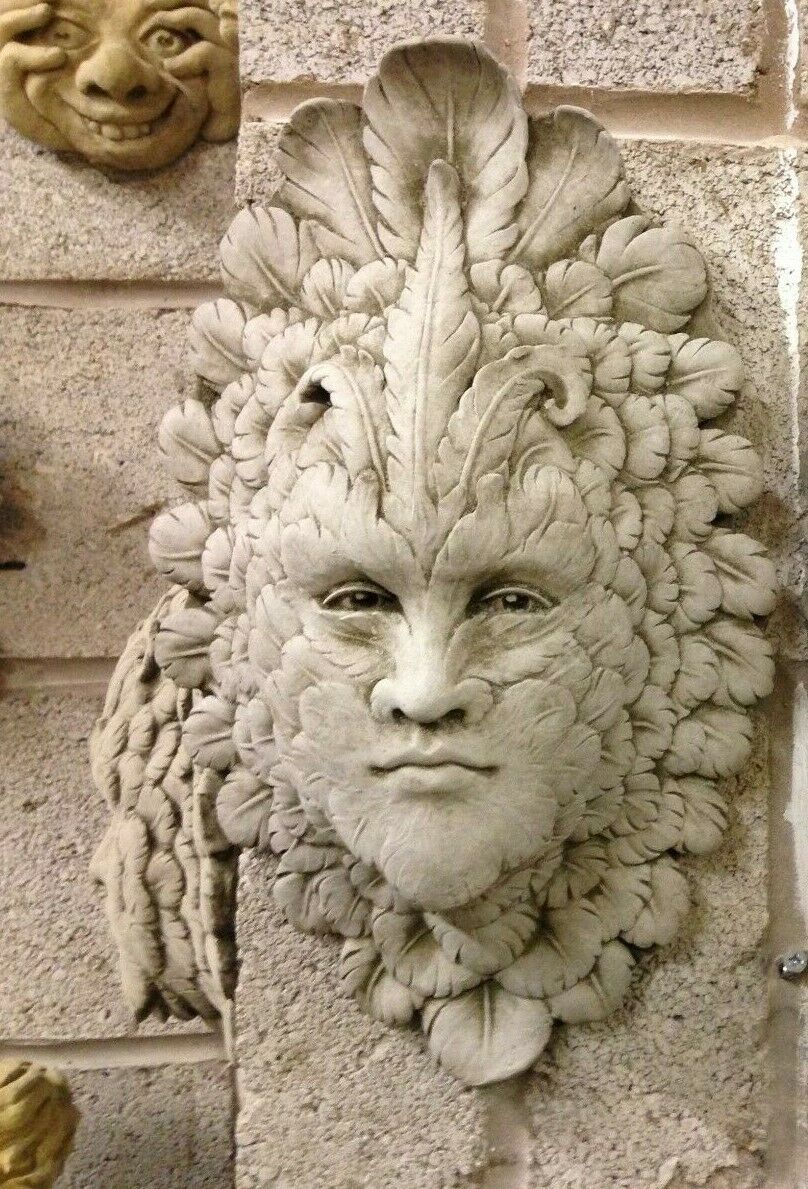 Full view of Greenman Wall Plaque - Stone Feather Face on textured wall. Celtic-inspired limestone plaque for garden or home display.