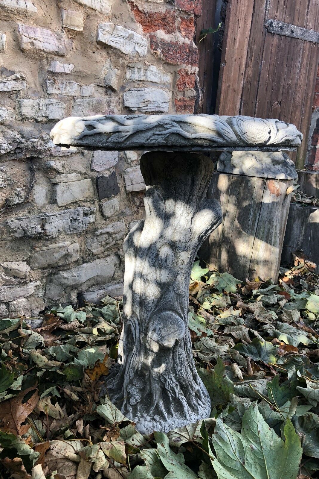 Stylish stone bird bath with carved tree trunk pedestal and textured bowl, enhancing rustic garden aesthetics.